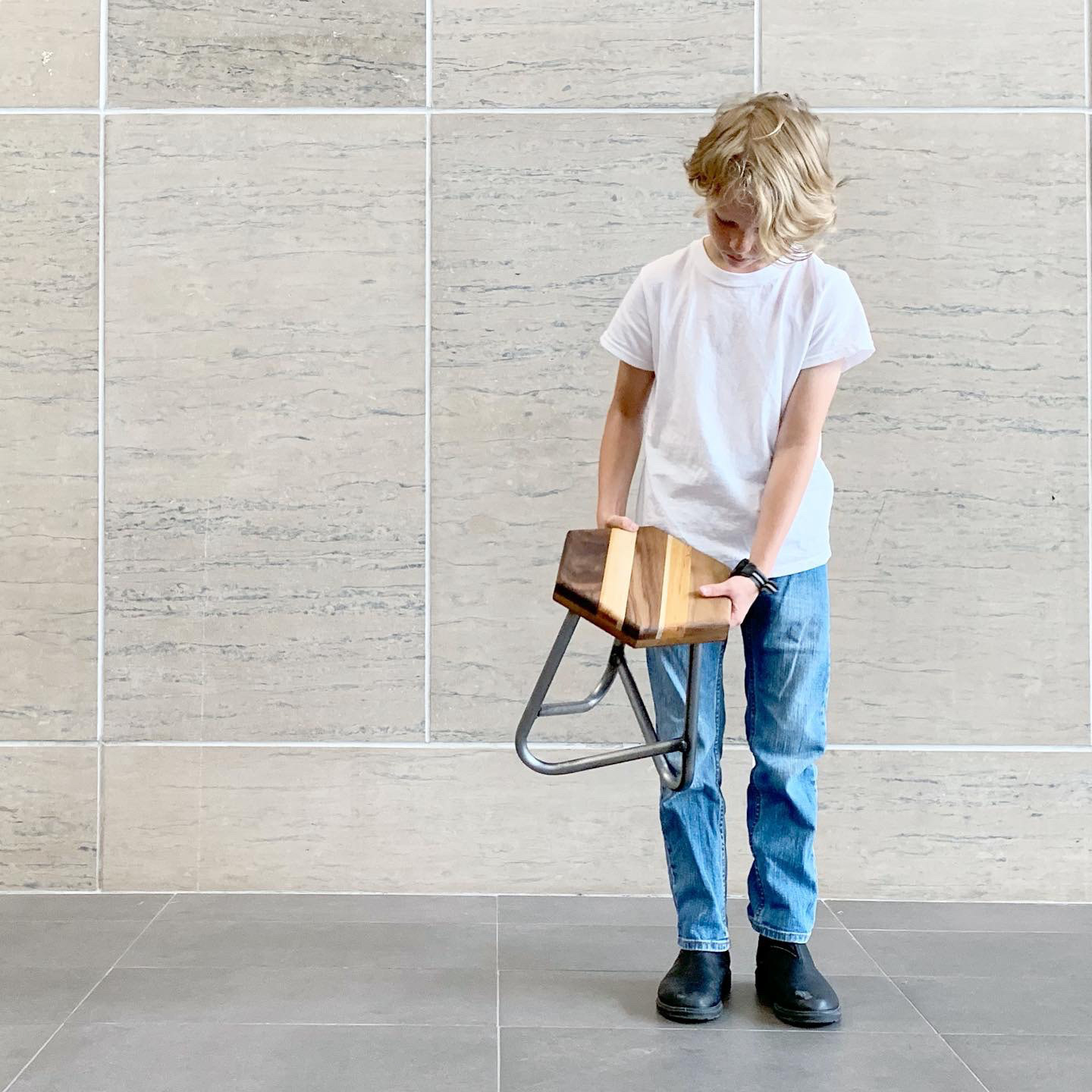 A child carries the stool by the seat.
