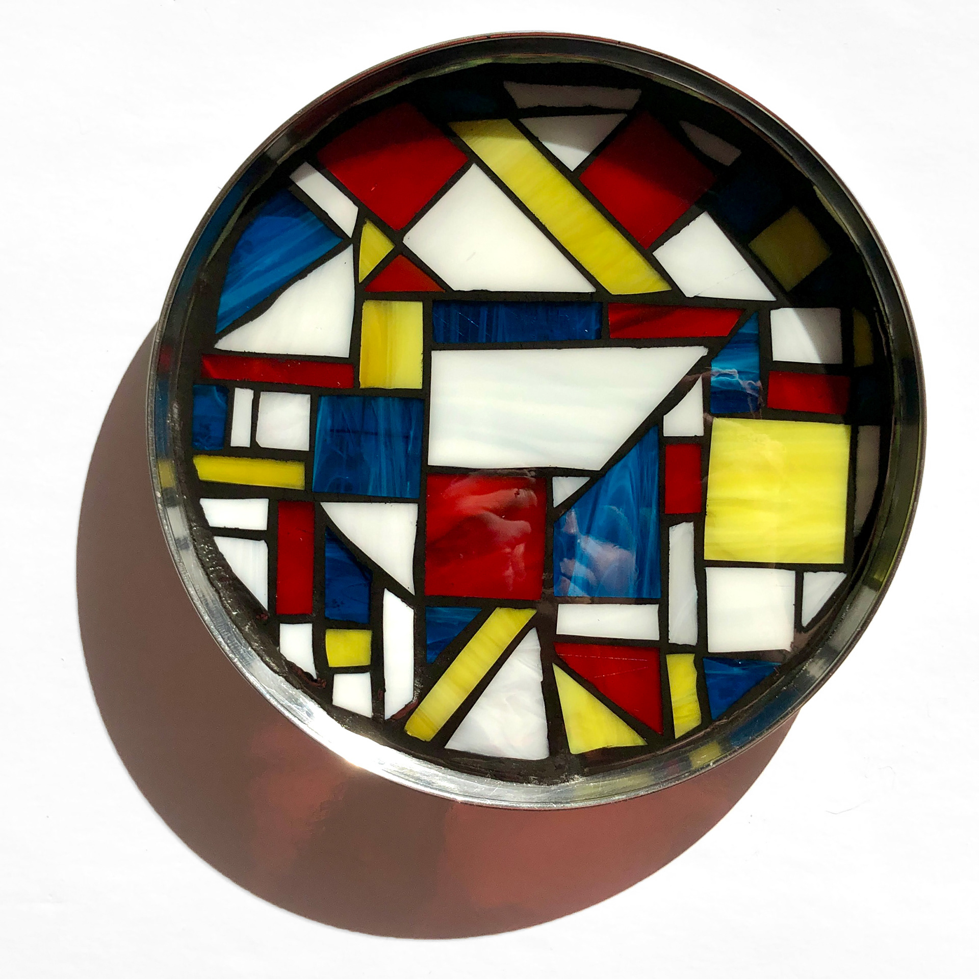 Finished tray with mosaics. Glass tiles are red, blue, yellow and white and are placed in a round silver dish. Grout separates the glass tiles.