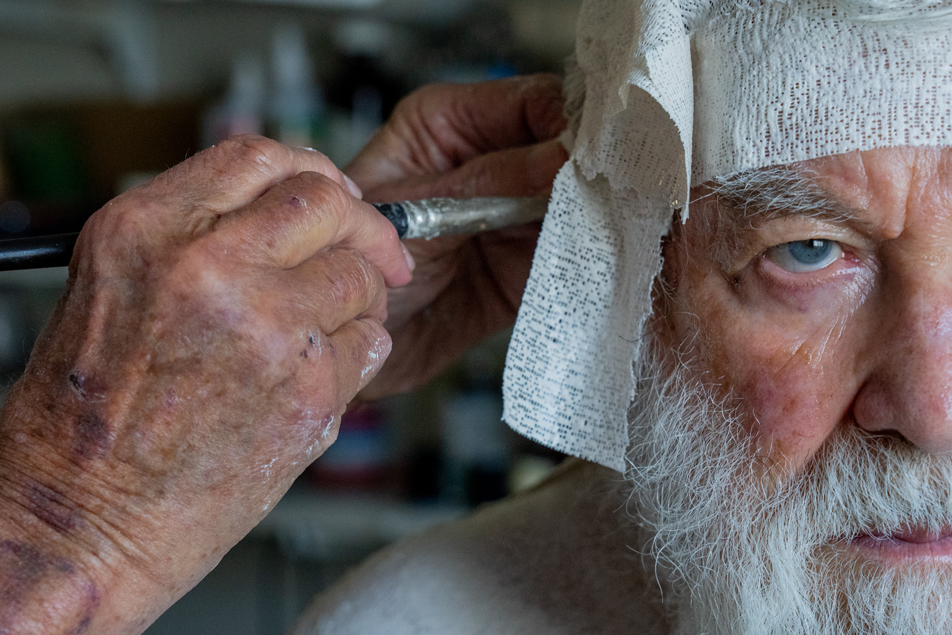 With the help of a paint brush, Robert Sutz places a plaster bandage on Holocaust survivor Werner Salinger’s ear at his studio in Scottsdale on Feb. 12, 2022. (Photo by Samantha Chow/Cronkite News)
