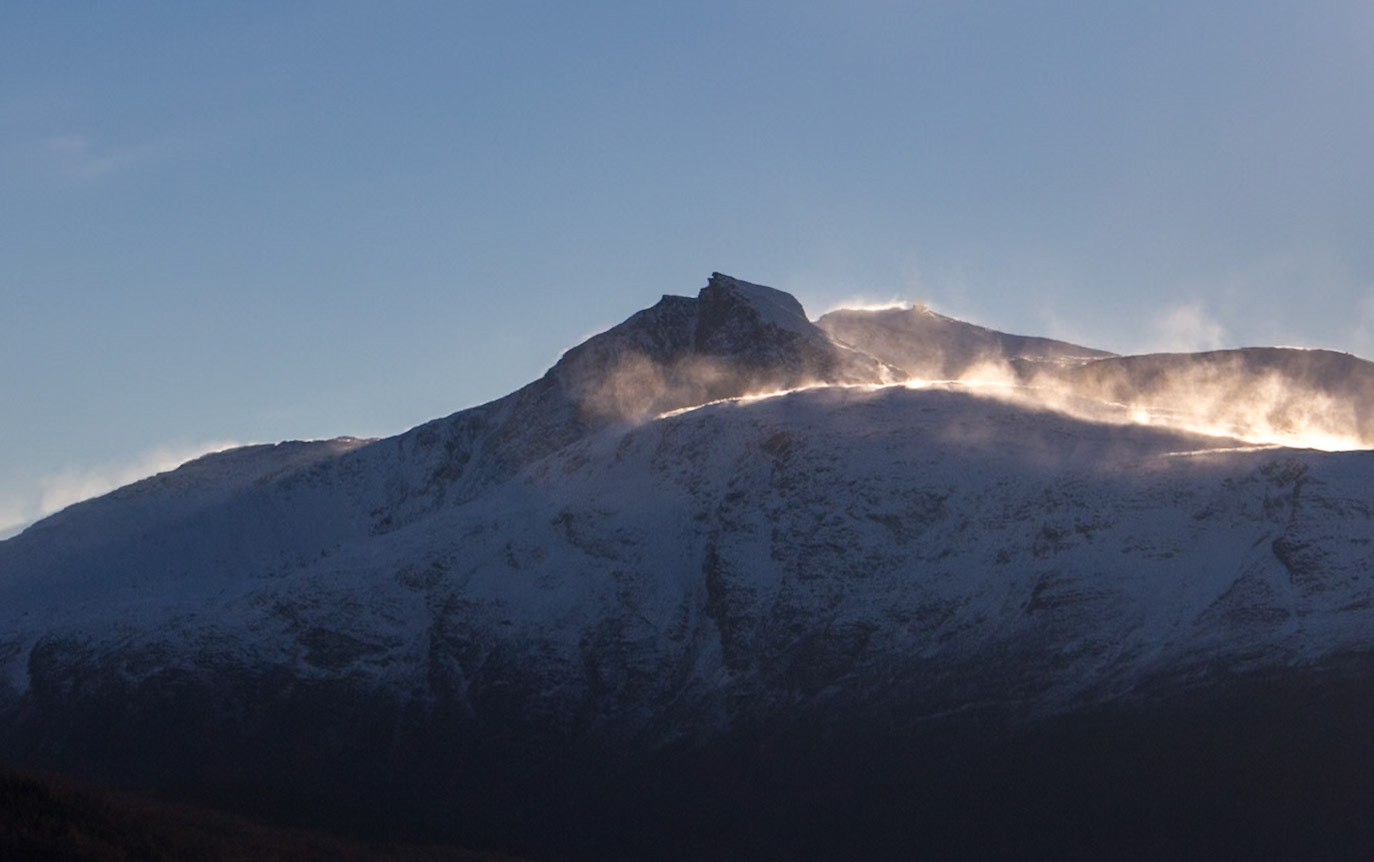 The low winter sun catching snow being blown from the mountain tops