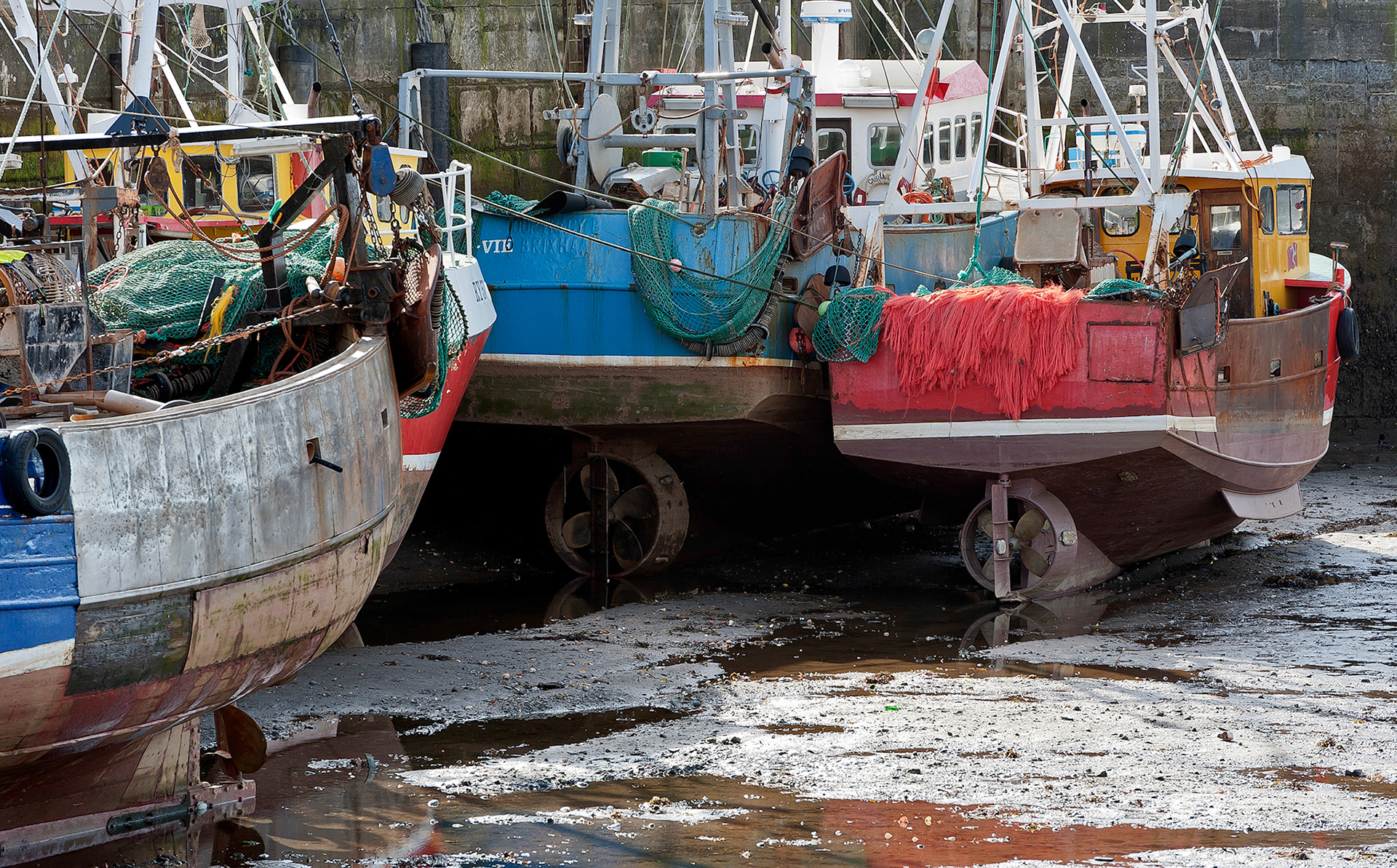 Fishing vessels line the harbour and rest in the mud during low tide at Ramsery Harbour on the Isle of Man in the North Atlantic.
