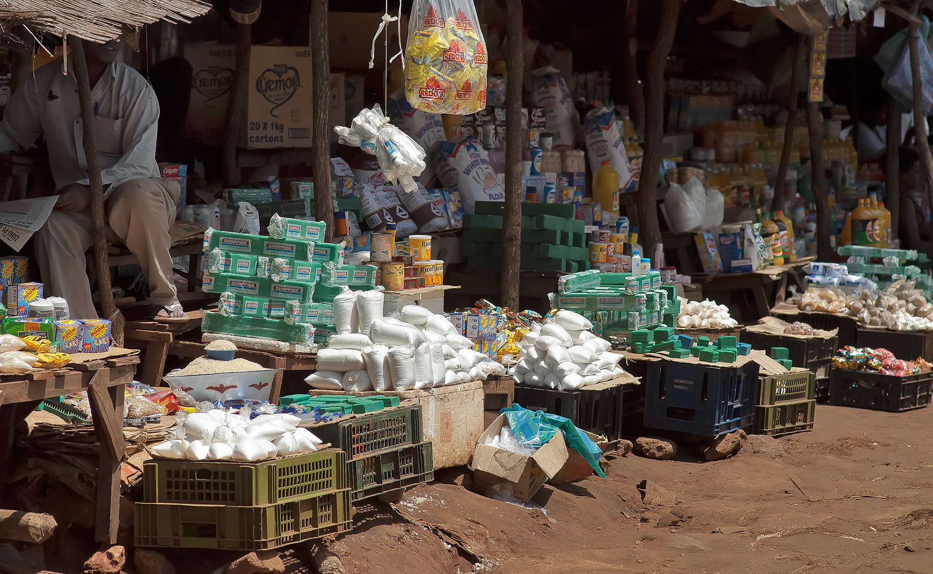 Stall owner looks up from his paper to keep an eye on the market and his goods.