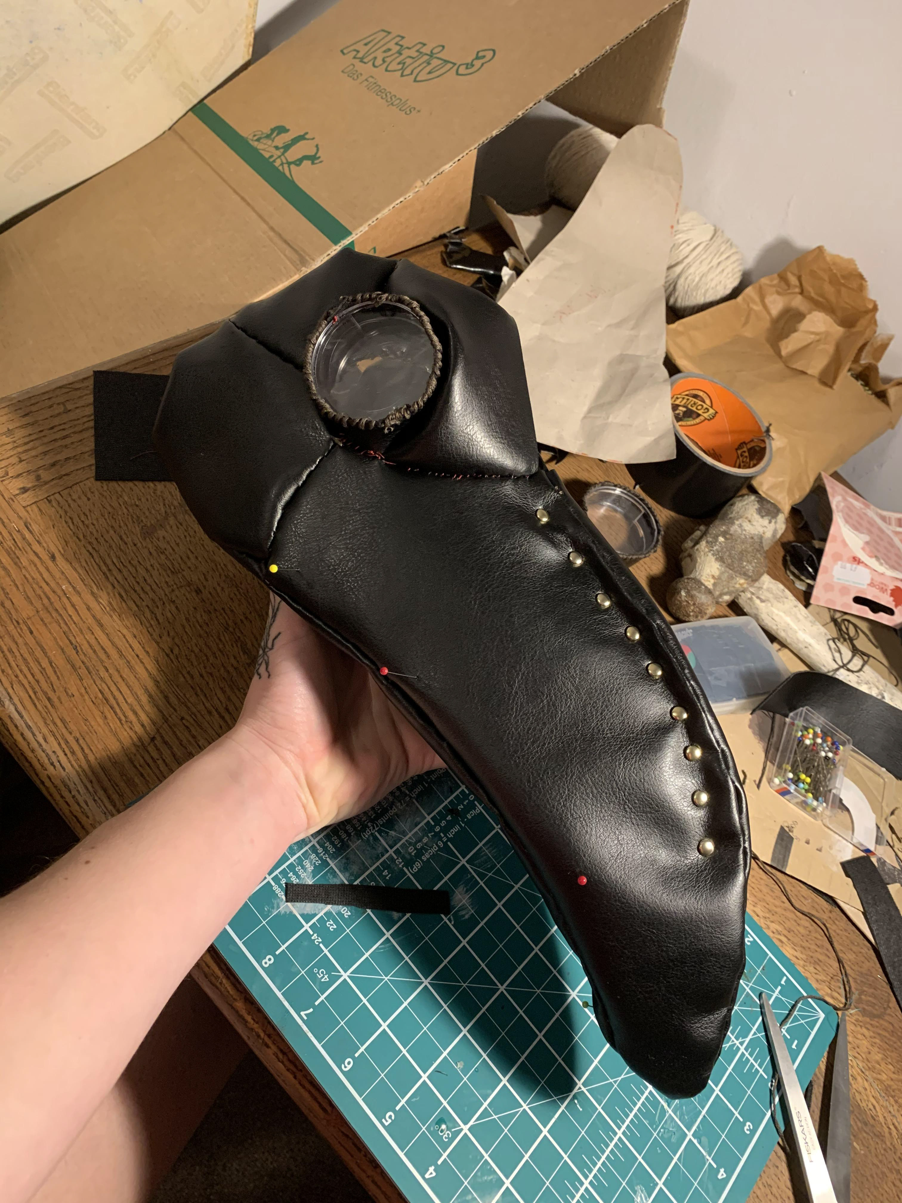 I carefully traced the shapes of the beak side profile, under the beak, sides of the face, around the eyes, and forehead onto black leather. Using embroidery thread, I sewed the pieces of the mask pattern directly onto the mask in order to secure the faux leather.