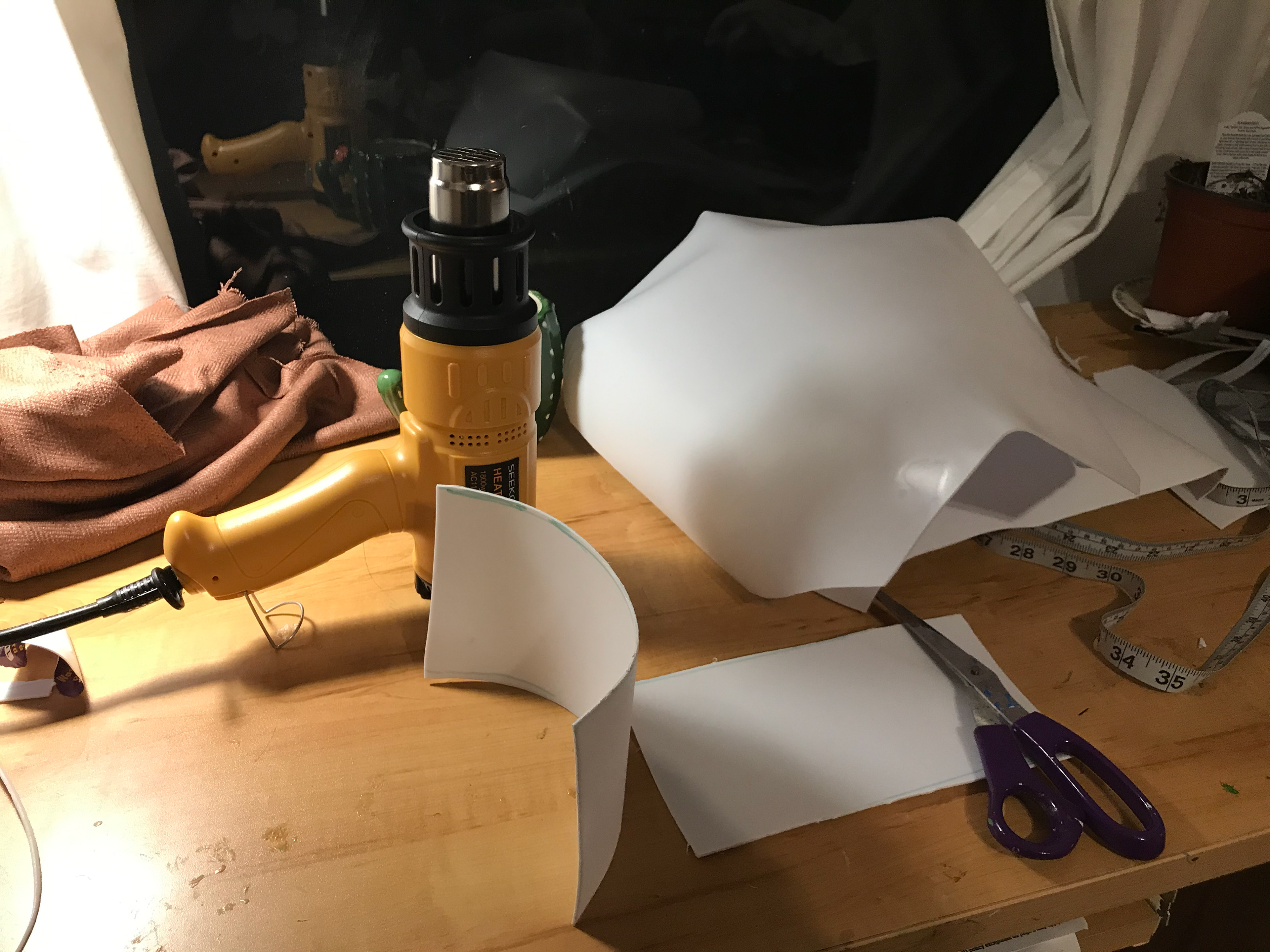 8. Using the plastic of a second trashcan, I cut two medium squares and began using the heat gun to heat them in the curve of shoulders. This was difficult because plastic does not naturally bend in a round way, and I needed to be very careful that I did not burn the plastic. I cut the shoulder pieces into a diamond shape after curving them enough, and finished by curving the edges inward.