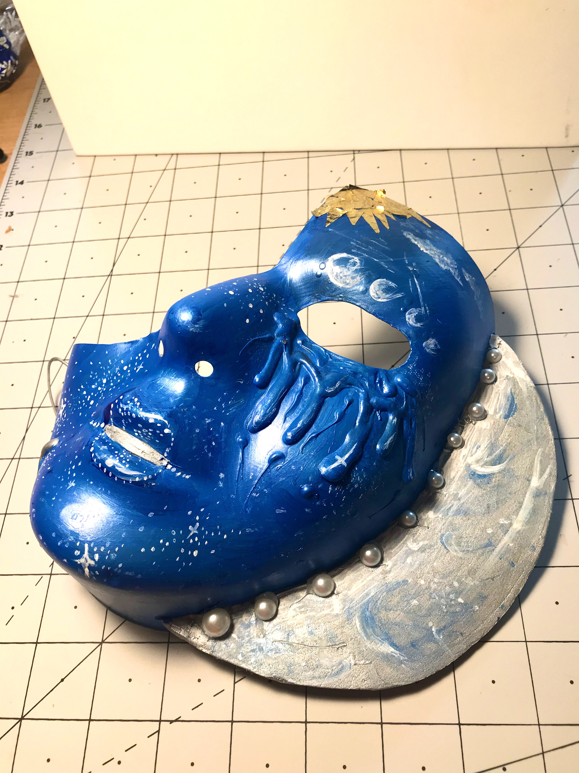 5. To connect the two masks further, I used gold foil in the left corners of the faces. With tweezers and modge podge, I carefully placed cut strips of gold foil to create the delicate shape of the sun on the moon mask.