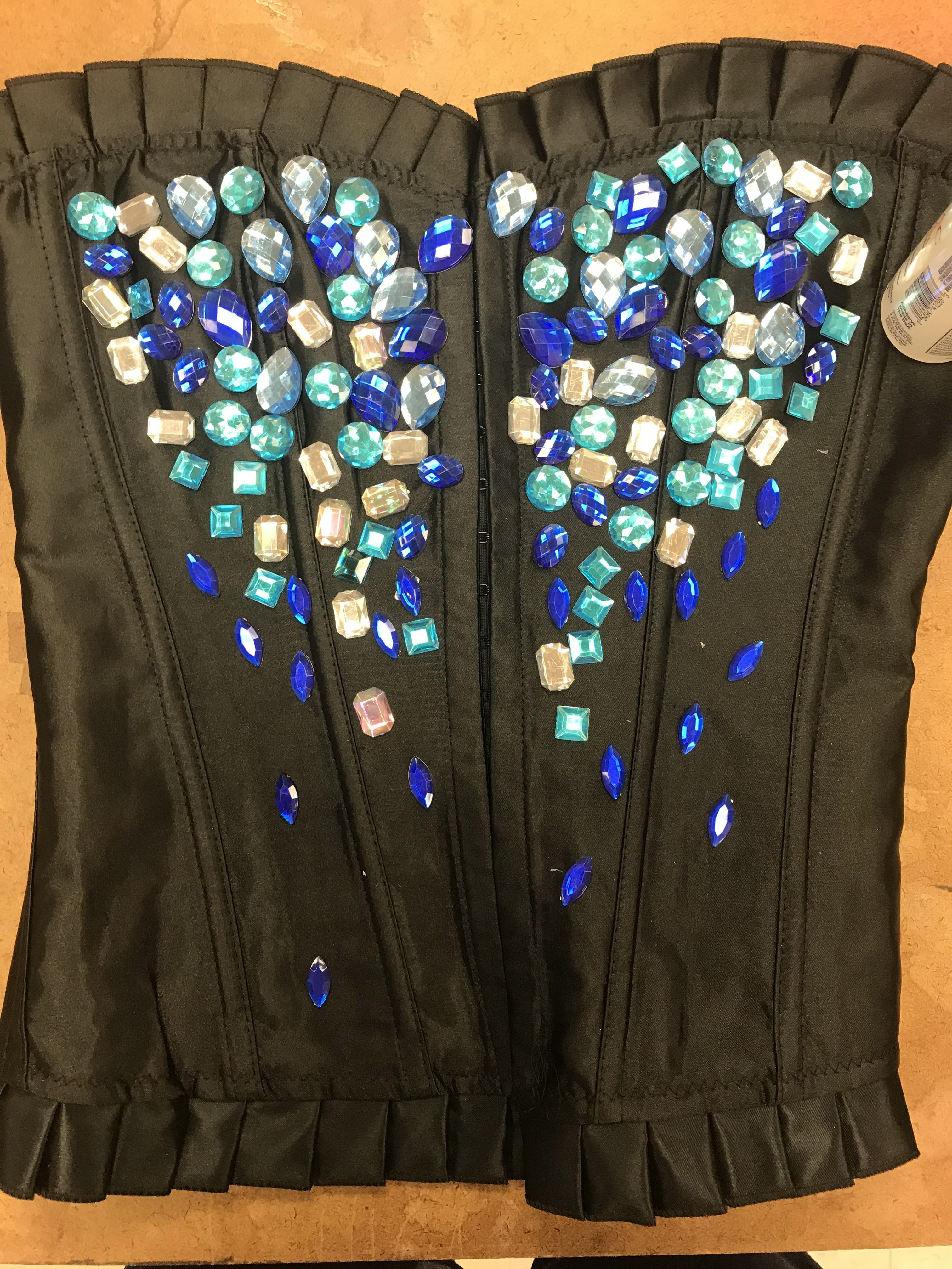 Our costume director ordered black corsets for the costumes and bags of plastic gems for the front of the corset. On the costume crew, we fabric tacked these gems to the fabric and altered the sizing of the corsets to fit the actresses we were assigned to. For the feather cages, we sewed feather boas to the empty cages and layered them in order to make the cages full. We fabric tacked black thin feather boas to the crest of the corsets, and sewed the cages onto the sides of the corsets. Lastly, we sewed white gem crotch curtains to the front of the cosets.