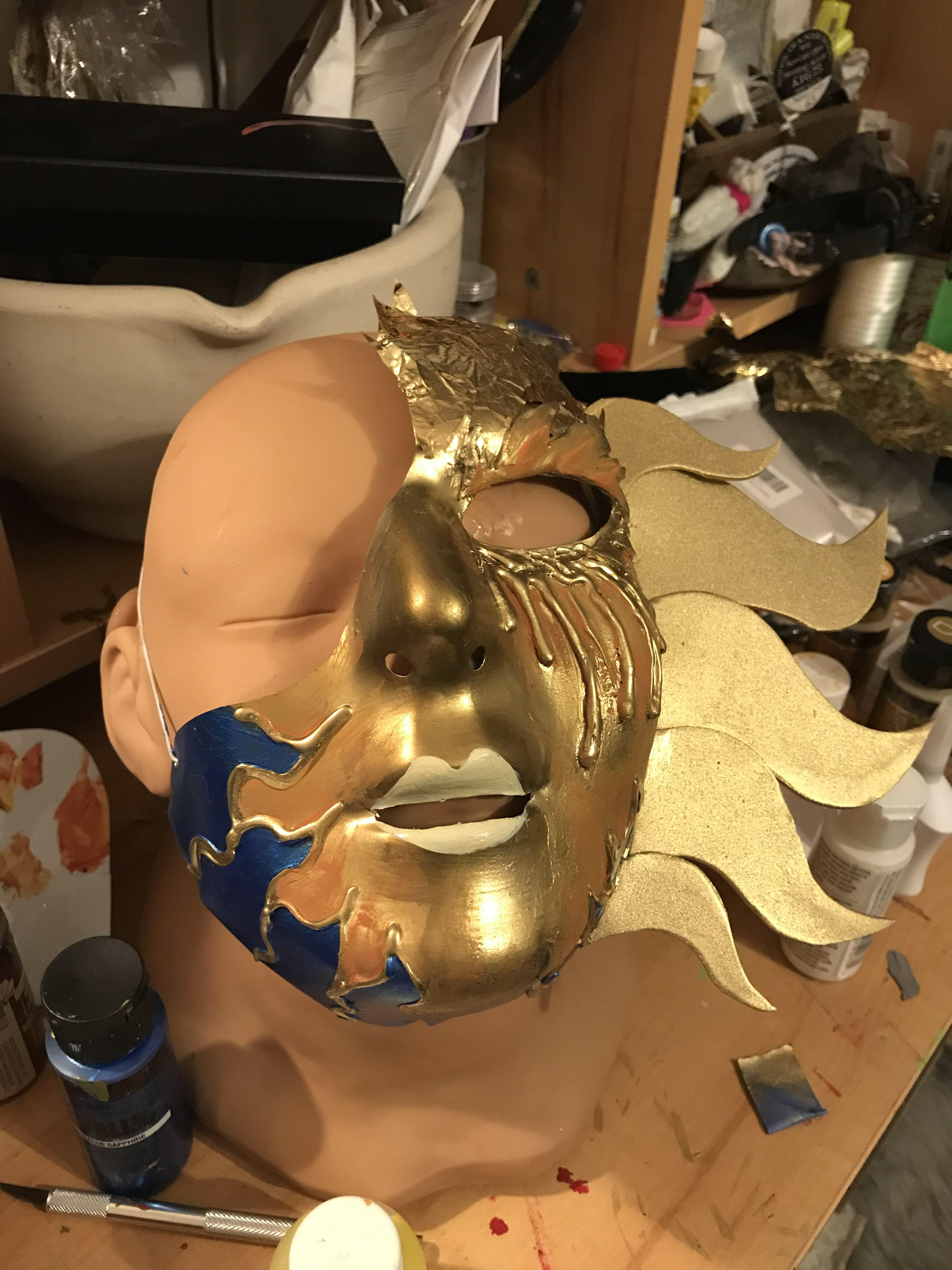 2. To create more drama in the masks, I cut craft foam pieces to add to the side of the face for both masks, and form the flared eyebrow for the sun mask. I hot glued these foam pieces to the masks and painted them over with the metallic paint. Finally, for the details!