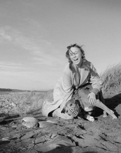 Amy in a black and white photo of a rocky beach, laughing with her old dog.