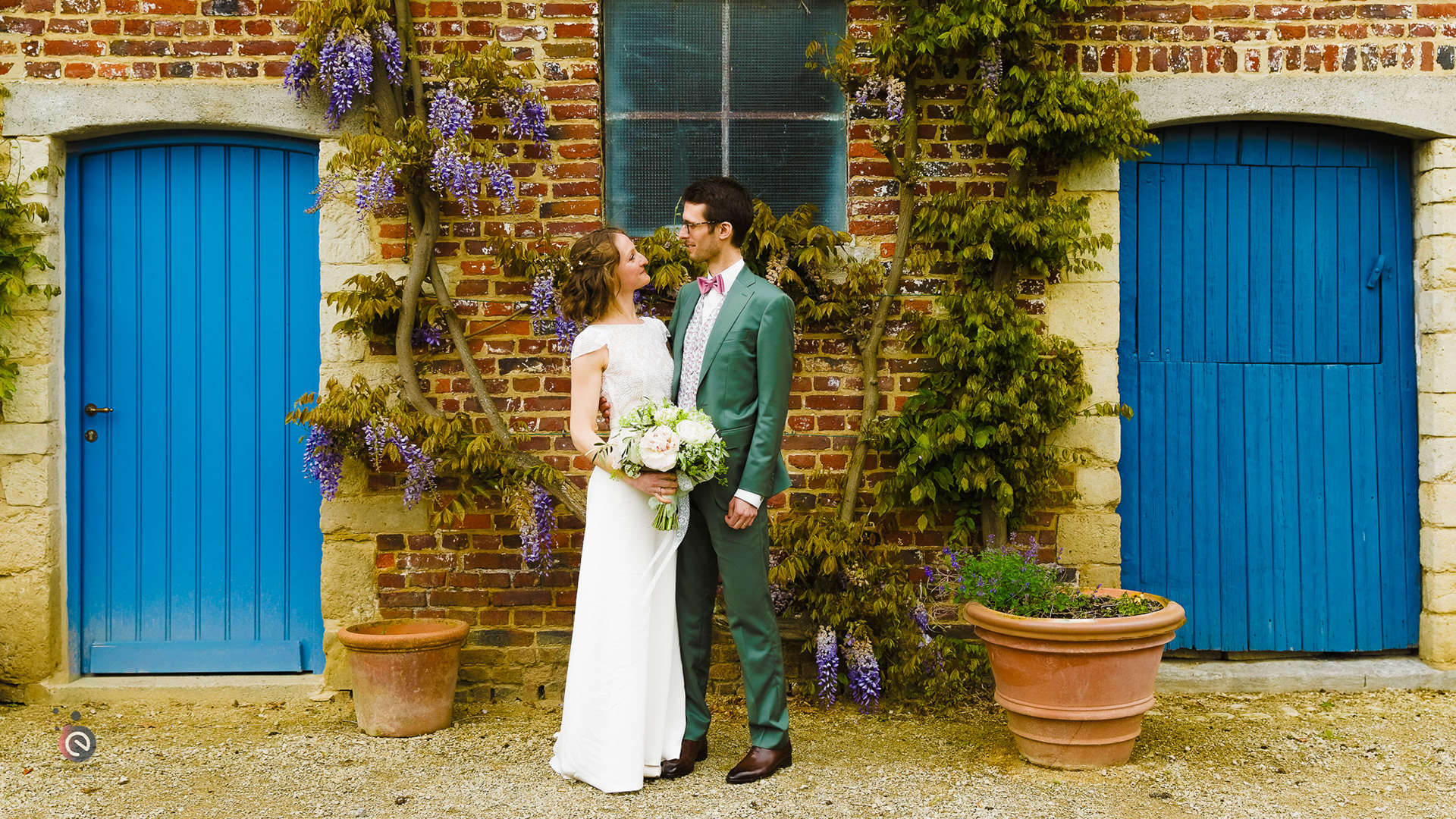 Chloé et Adrien posant devant les façades fleuries de la ferme de Corroy-le-Grand lors de leur mariage en Belgique – organisation par event your life.