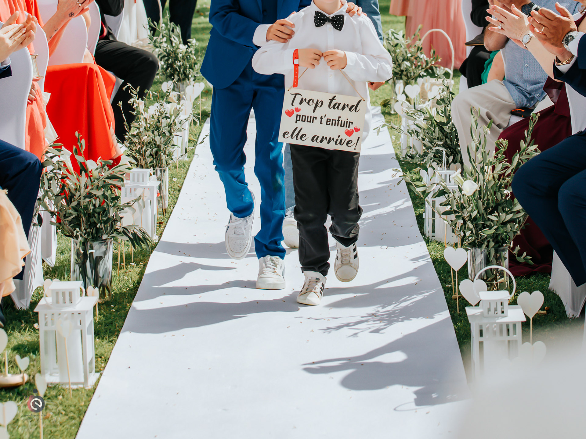 Allée de cérémonie de mariage décorée de lanternes et d’oliviers, accompagnée par des enfants d’honneur — organisation et décoration de mariage en Belgique.