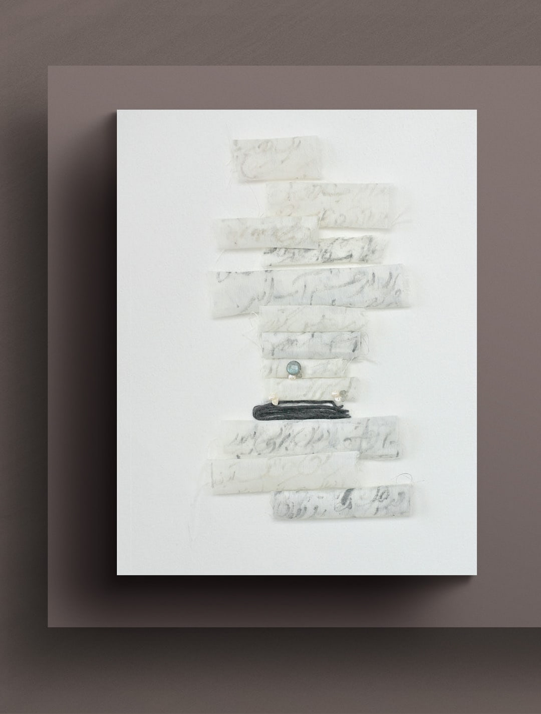 full view of 12 Poem Scrolls art on mauve gallery wall The fuzzy wool yarn, with its dusky graphite color, sets off a sharp contrast against the elegant intricacy of labradorite gemstone and pearls