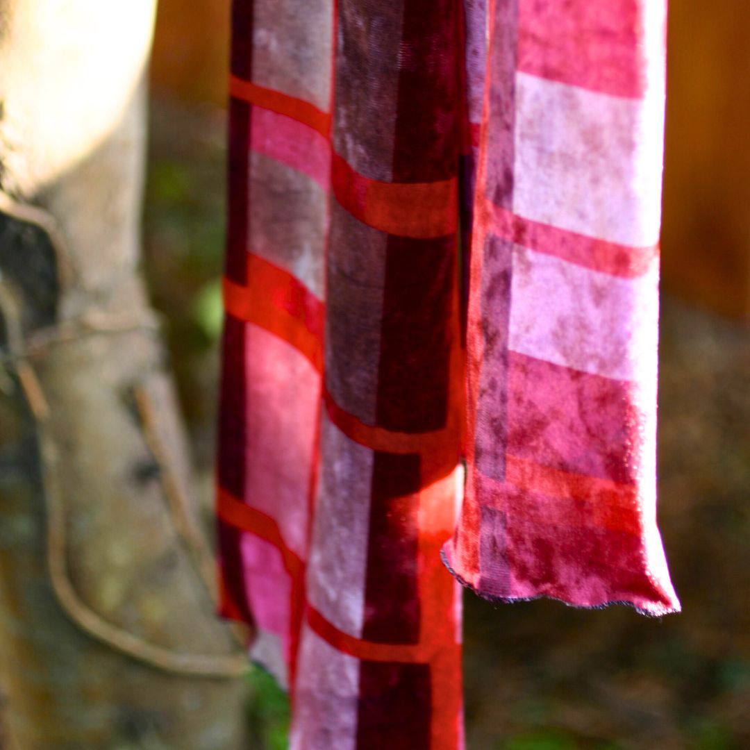 A deep wine red geometric scarf hanging from a sunlit tree.