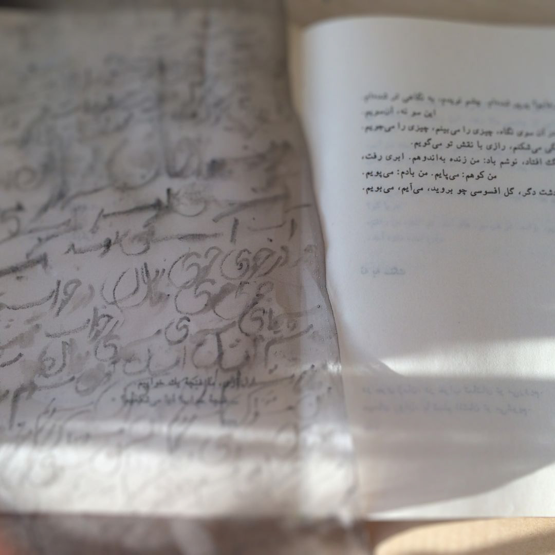 an open book of Persian poetry and a sheer fabric showing hand inscription