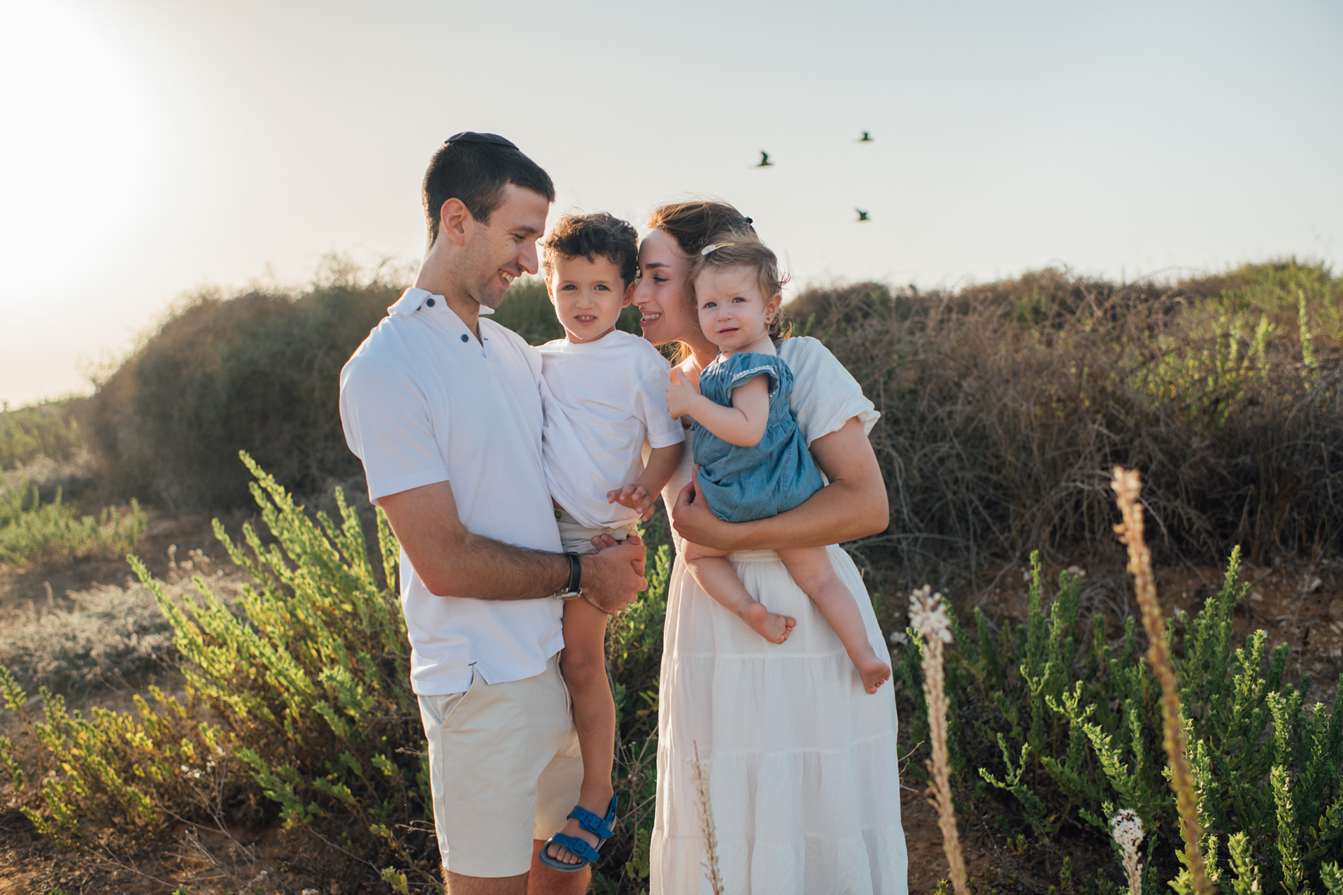 Family photo, mom, dad holding two kids, open field and birds flying behind