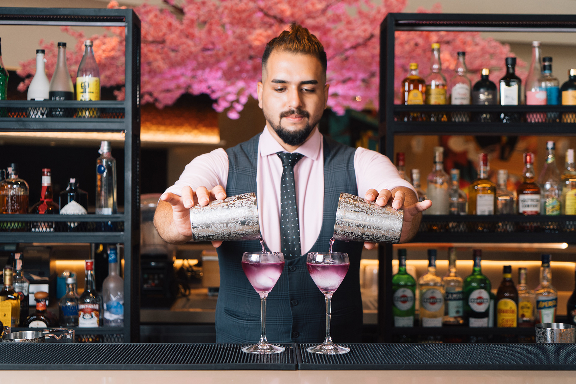 The bartender is pouring a cocktail into a glass.