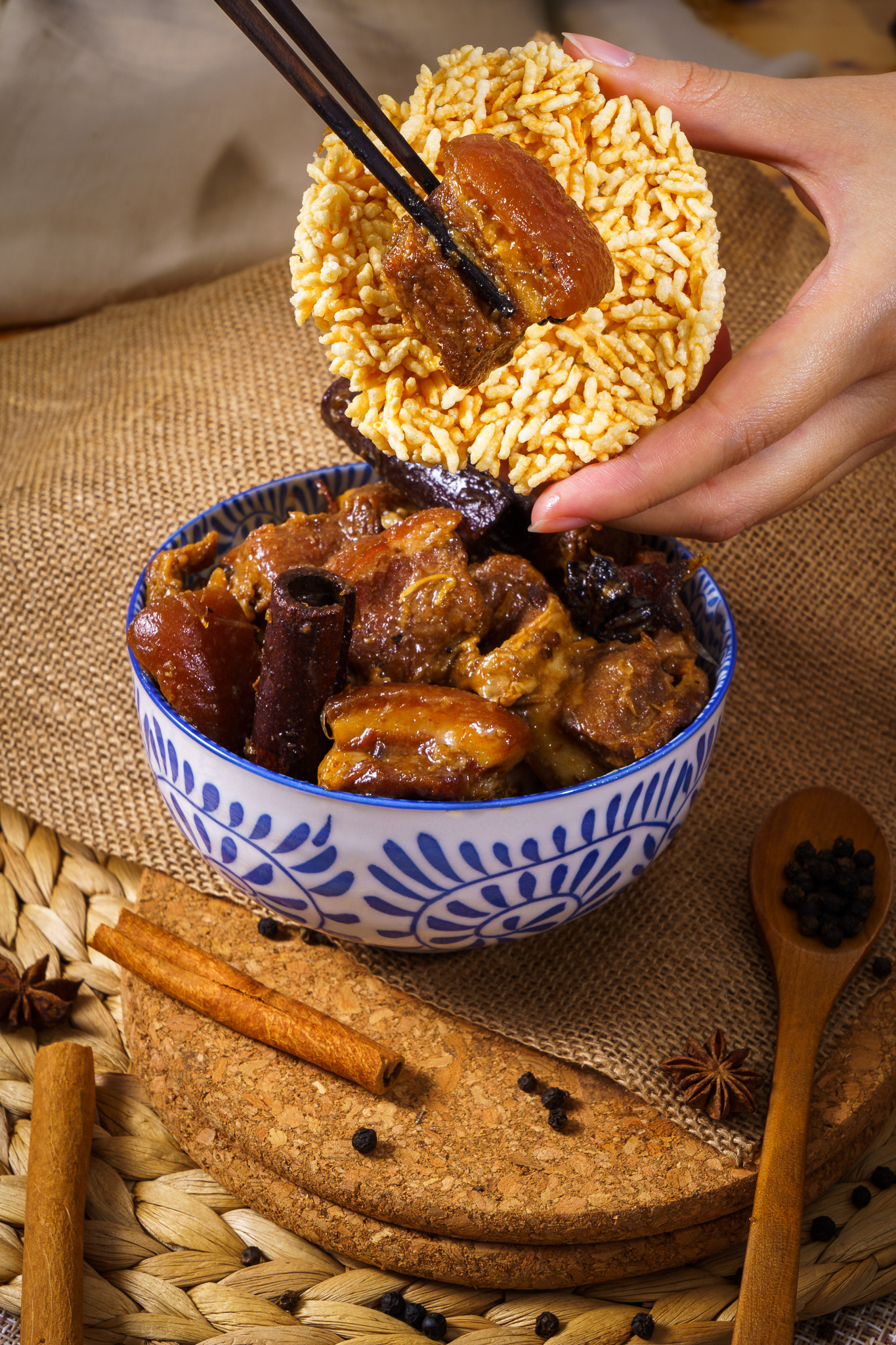 Hand of people using wood chopsticks holding stewed pork in white bowl with Thai rice cracker 