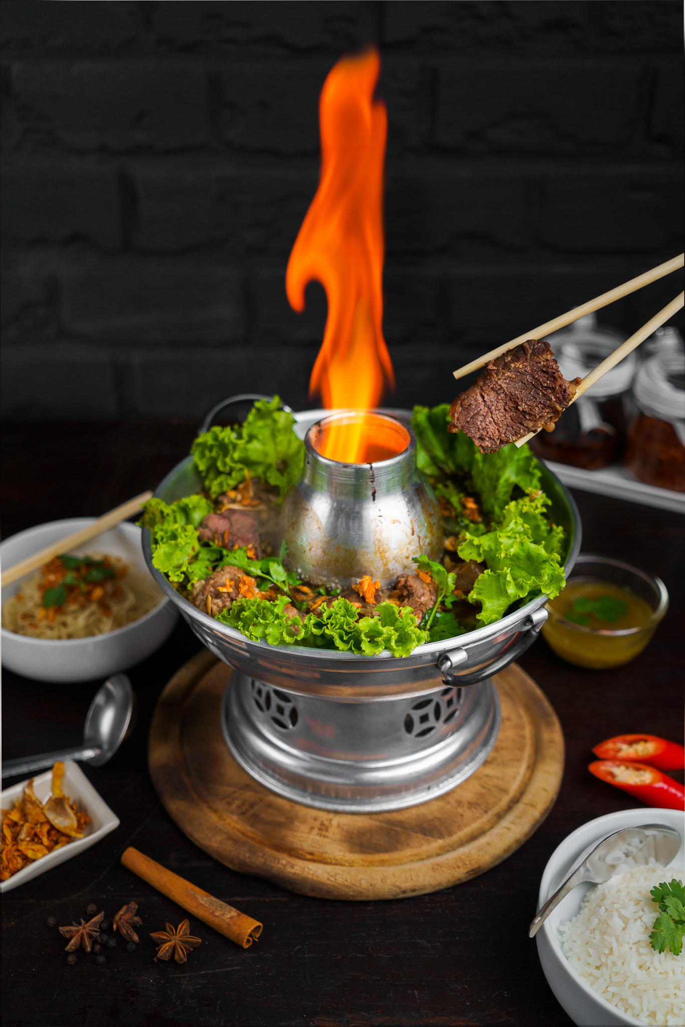 Hand of people using wood chopsticks holding braised beef with beef tripe, meatball and vegetable in Thai beef soup on fire hot pot with wooden table