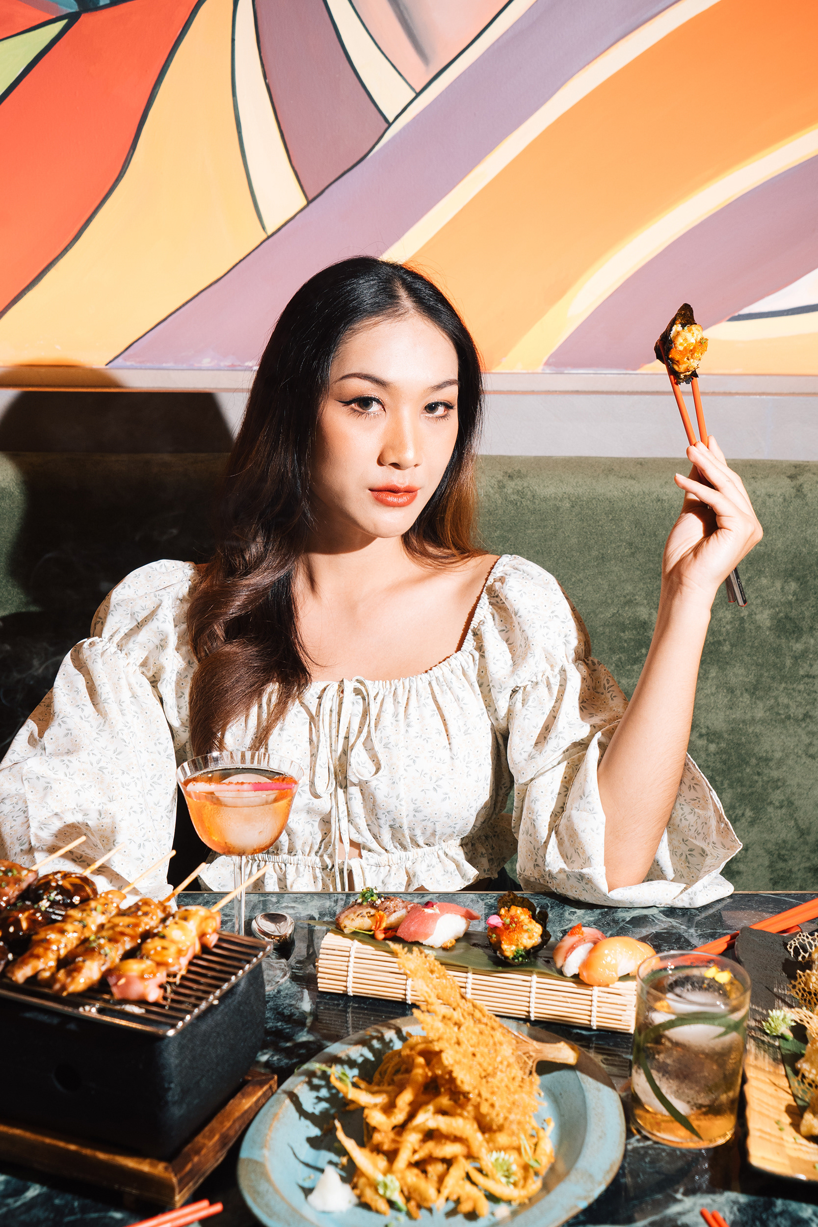 Model holding sushi with lots of Japanese food on the table