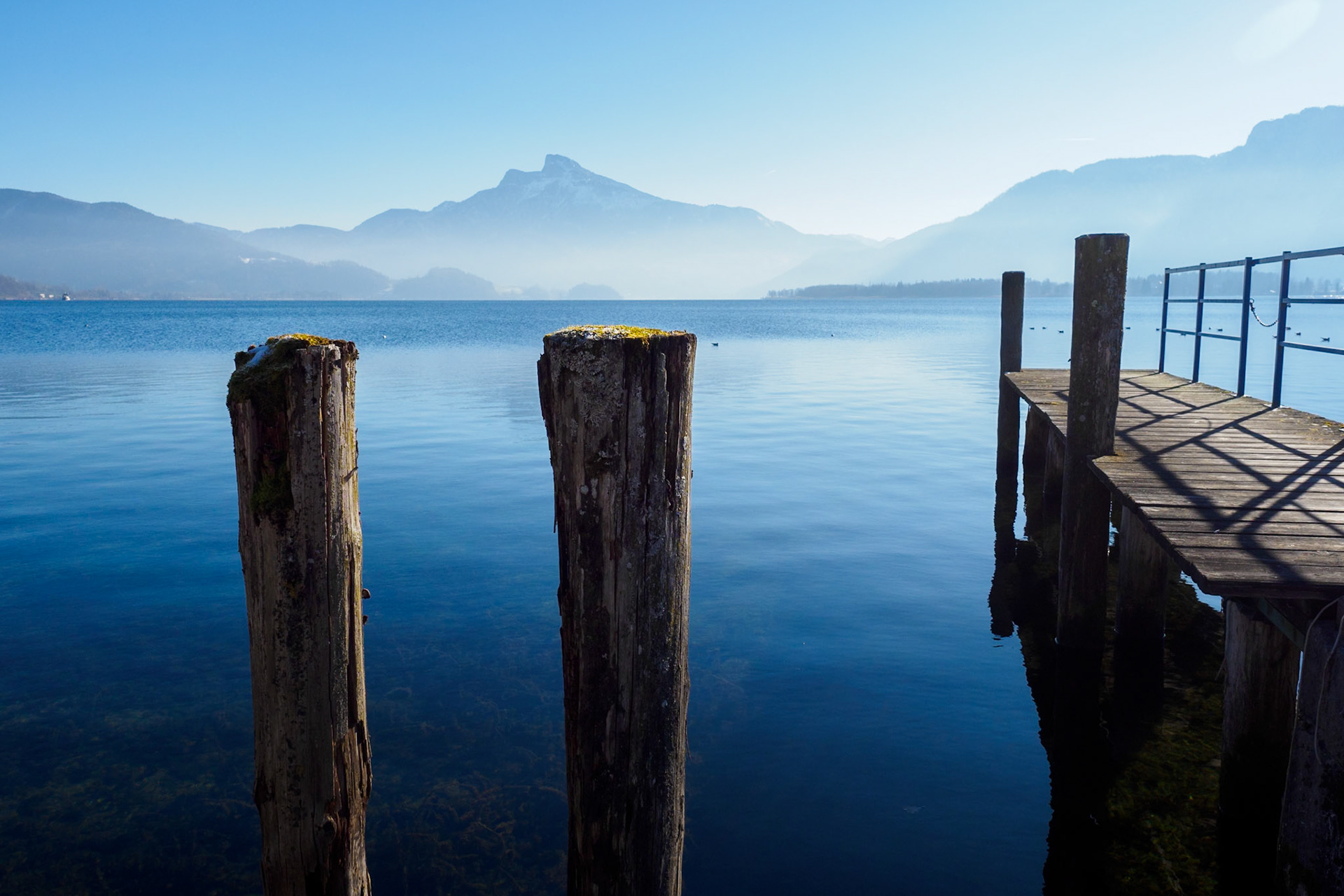 weathered wooden posts and pier extending into calm, reflective waters of Mondsee, Austria