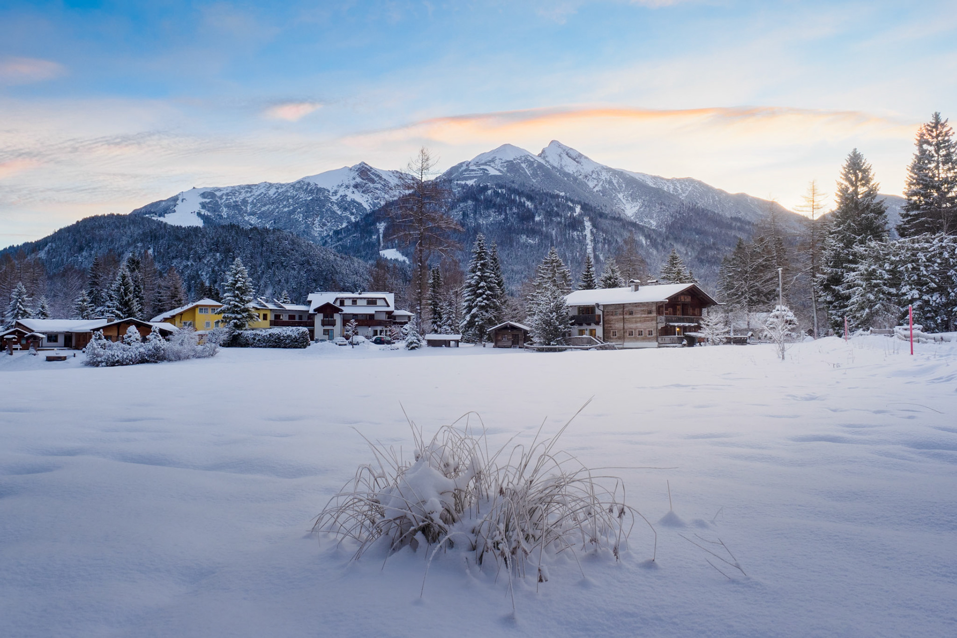 The golden hour light over the Alps illuminates a serene village scene. Shot at Seefeld, Austria, in December.