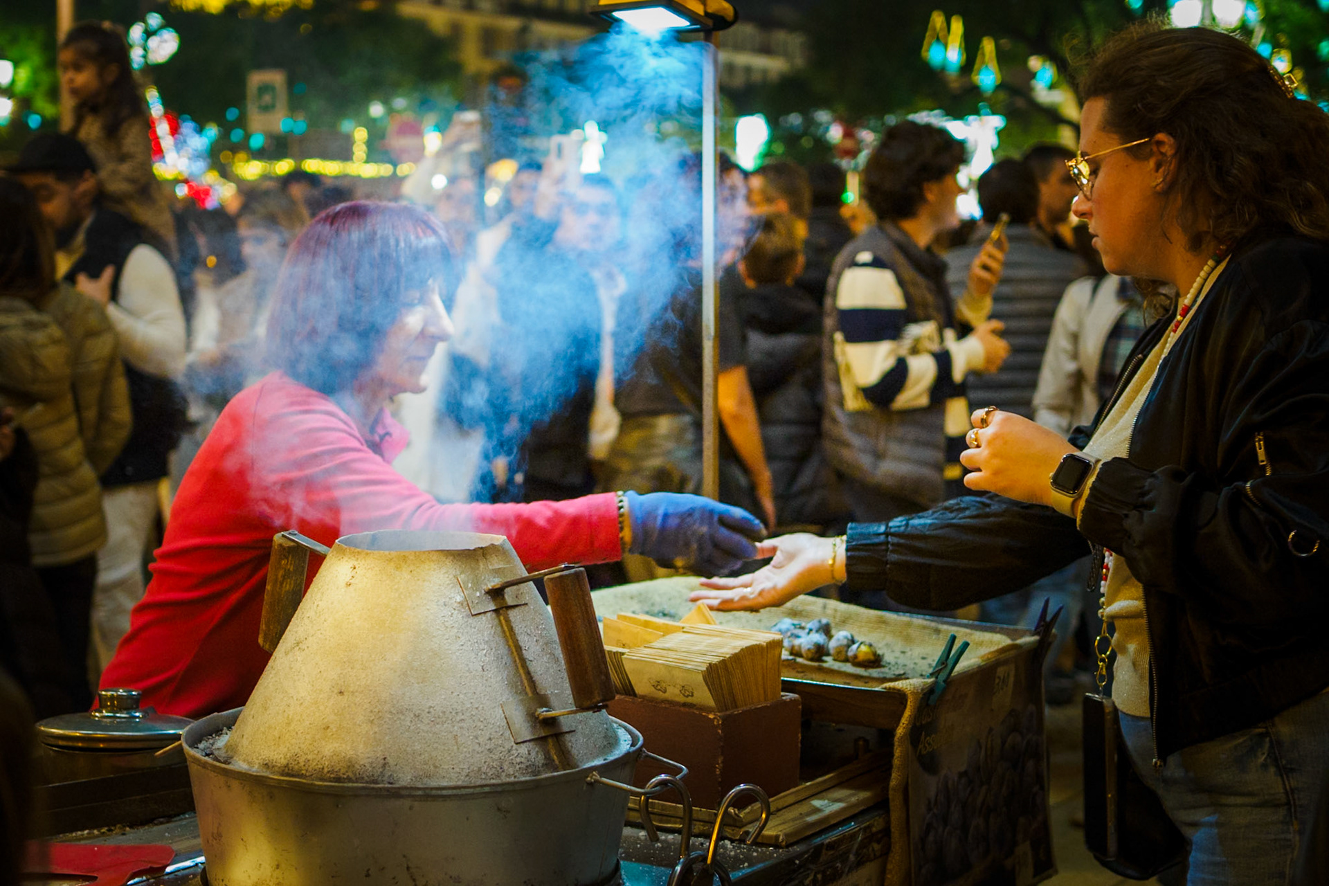A street vendor sells hot roasted chestnuts in Lisbon in winter, near a Christmas market.