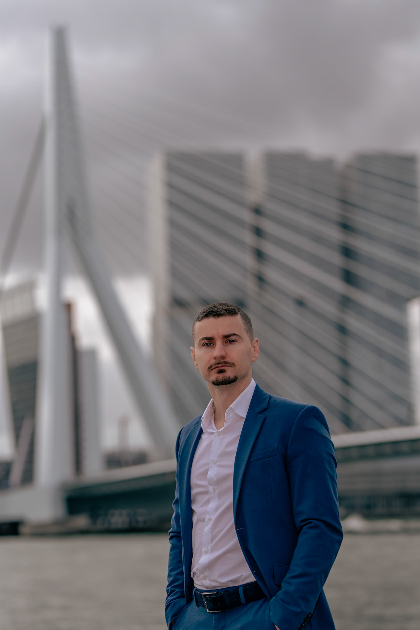 Zakelijk portret man, buiten gefotografeerd met de Erasmusbrug in Rotterdam op de achtergrond.