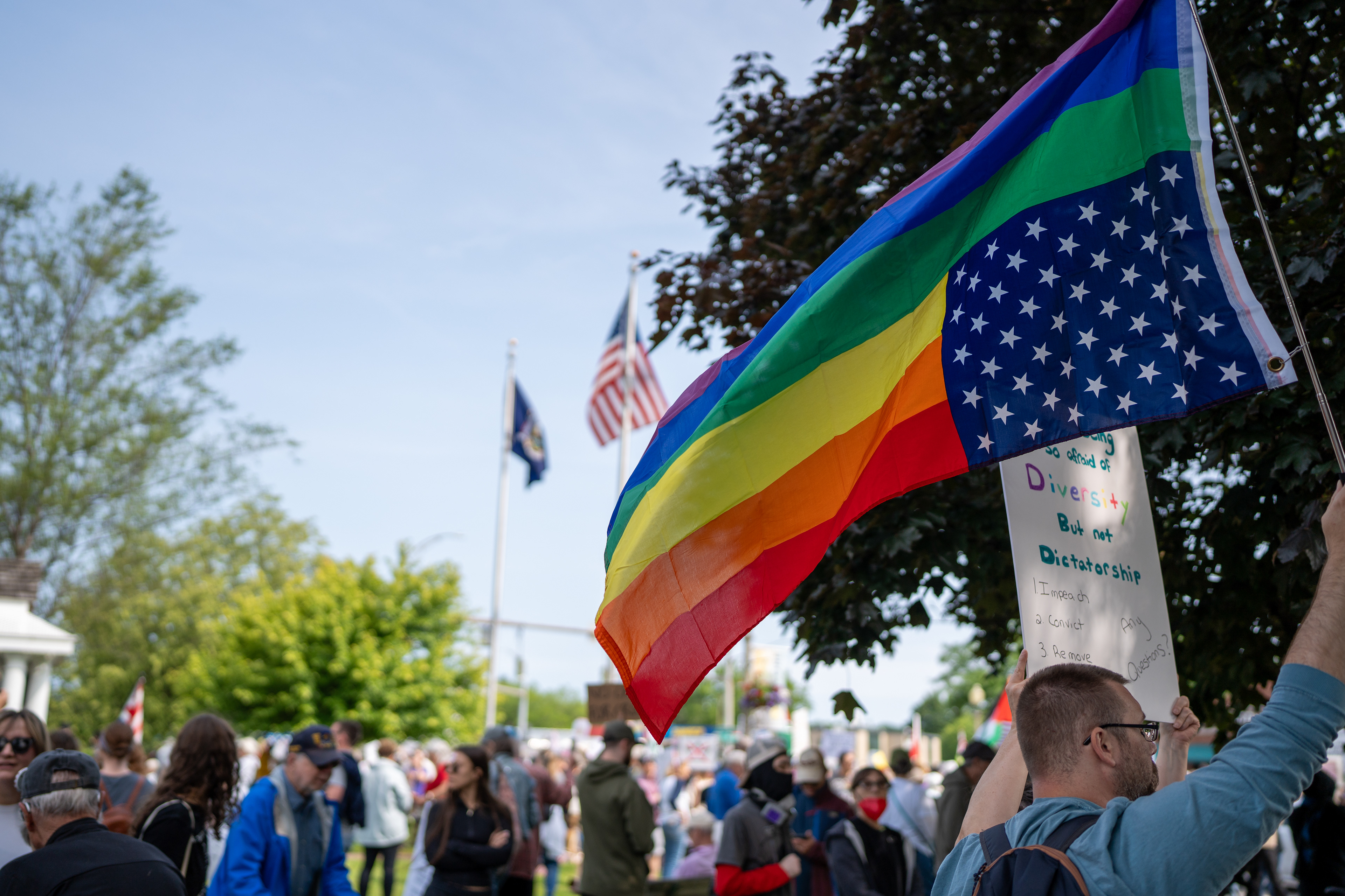 A demonstrator holds an upside-down American flag with rainbow stripes at the Twelve Corners intersection during a No Kings protest in Brighton, N.Y., Saturday, June 14, 2025.