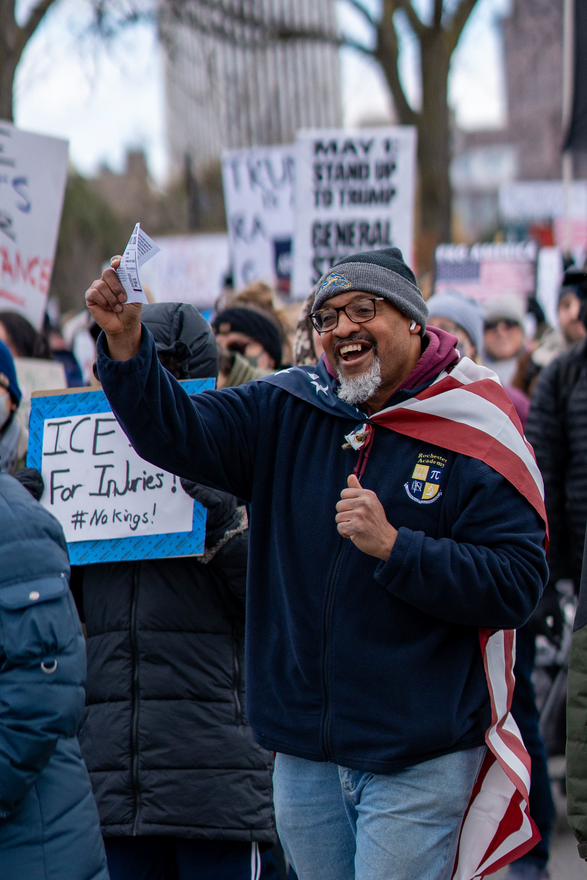 A demonstrator wearing an American flag as a cape cheers during a No Kings march from Genesee Gateway Park in Rochester, N.Y., Saturday, March 28, 2026.