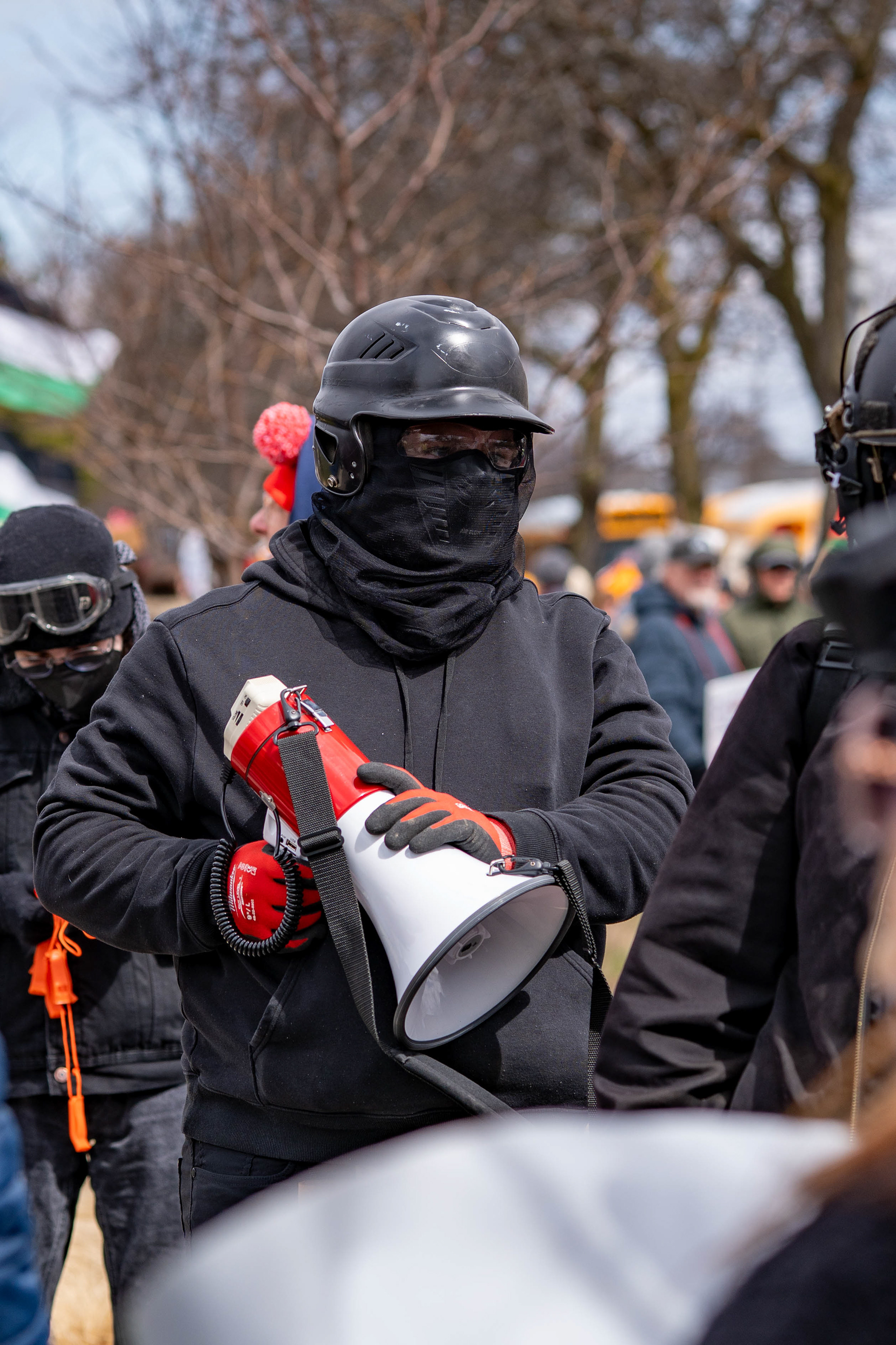 A masked demonstrator holds a megaphone during a confrontation with a counterprotester at Genesee Gateway Park in Rochester, N.Y., during a No Kings protest, Saturday, March 28, 2026.