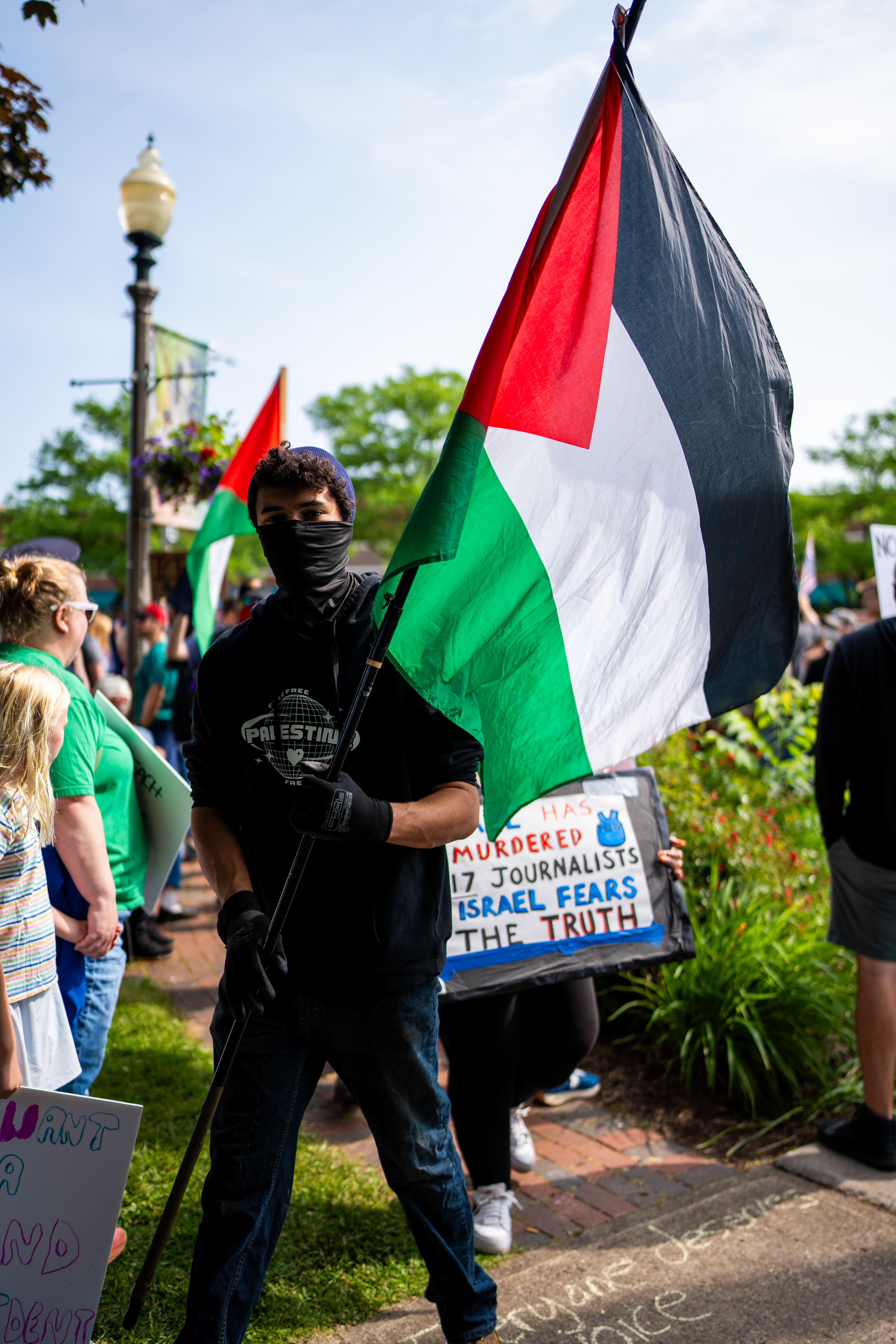 A masked demonstrator waves a Palestinian flag at the Twelve Corners intersection during a No Kings protest in Brighton, N.Y., Saturday, June 14, 2025.