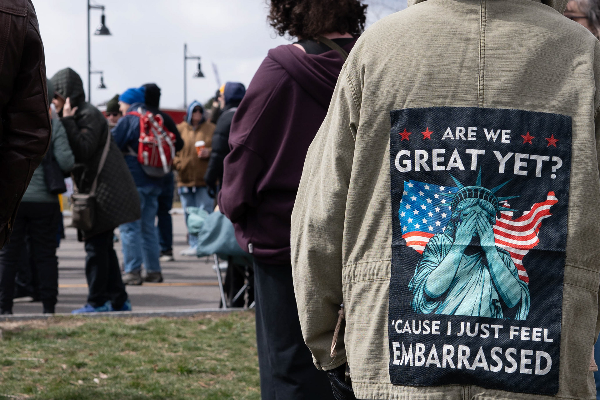 A demonstrator wears a jacket printed with the words “Are we great yet? ’Cause I just feel embarrassed” during a No Kings protest at Genesee Gateway Park in Rochester, N.Y., Saturday, March 28, 2026.