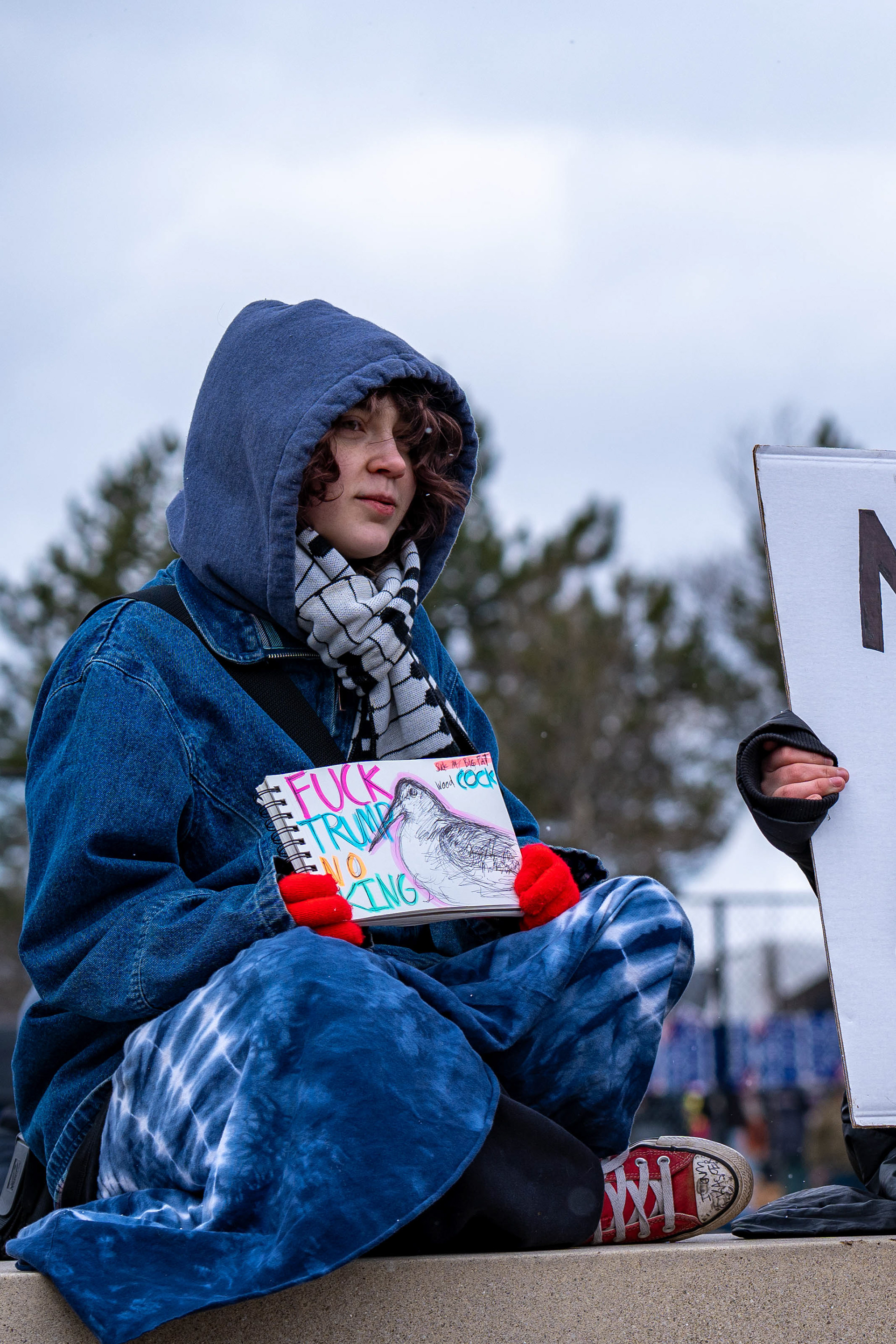 A demonstrator holds a sketchbook sign with a drawing of a woodcock and the words “F--- Trump, No Kings, suck my big fat Wood Cock” during a No Kings protest at Genesee Gateway Park in Rochester, N.Y., Saturday, March 28, 2026.