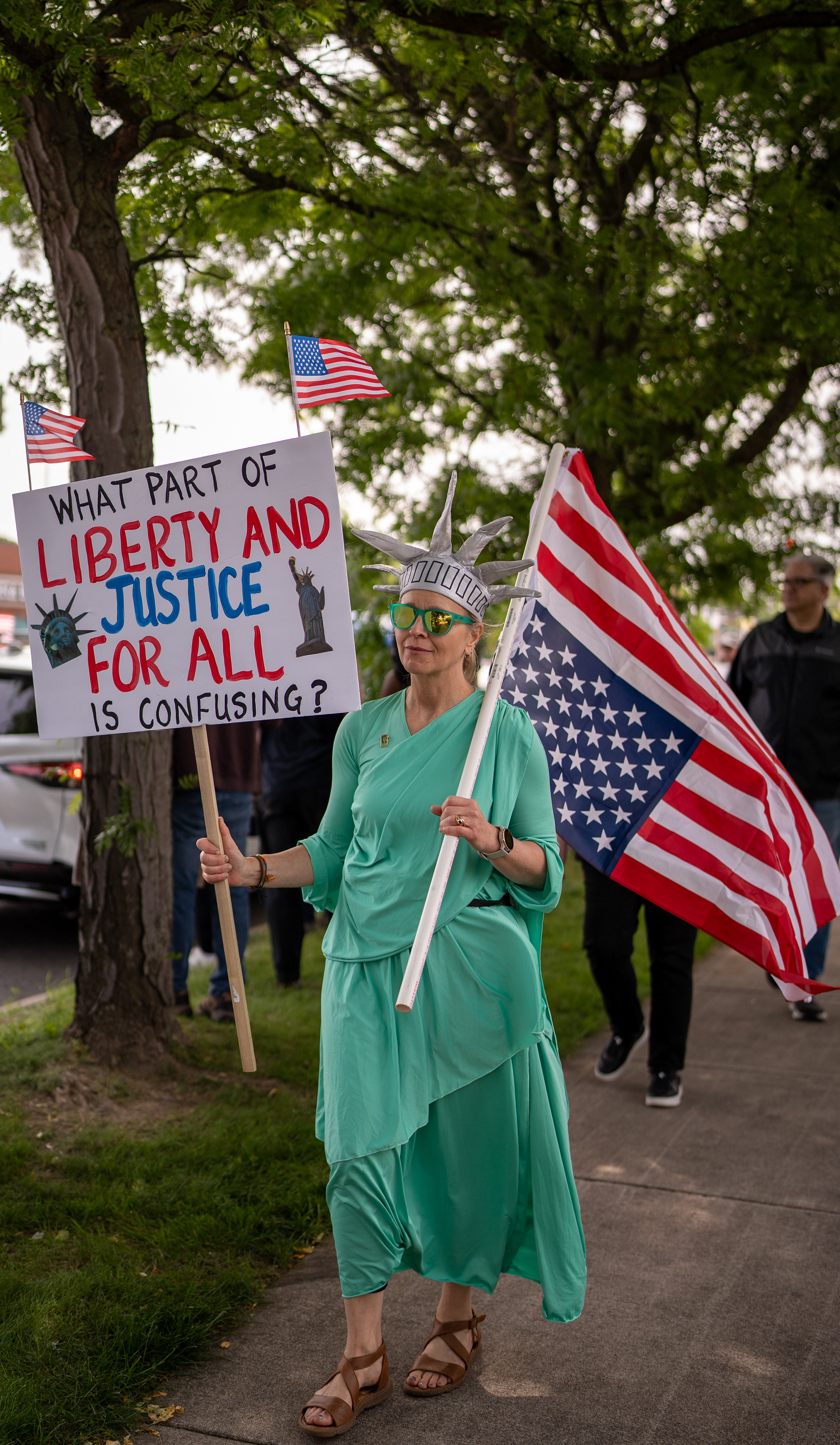 A demonstrator dressed as the Statue of Liberty holds a sign reading “What part of liberty and justice for all is confusing?” and an upside-down American flag at the Twelve Corners intersection during a No Kings protest in Brighton, N.Y., Saturday, June 14, 2025.
