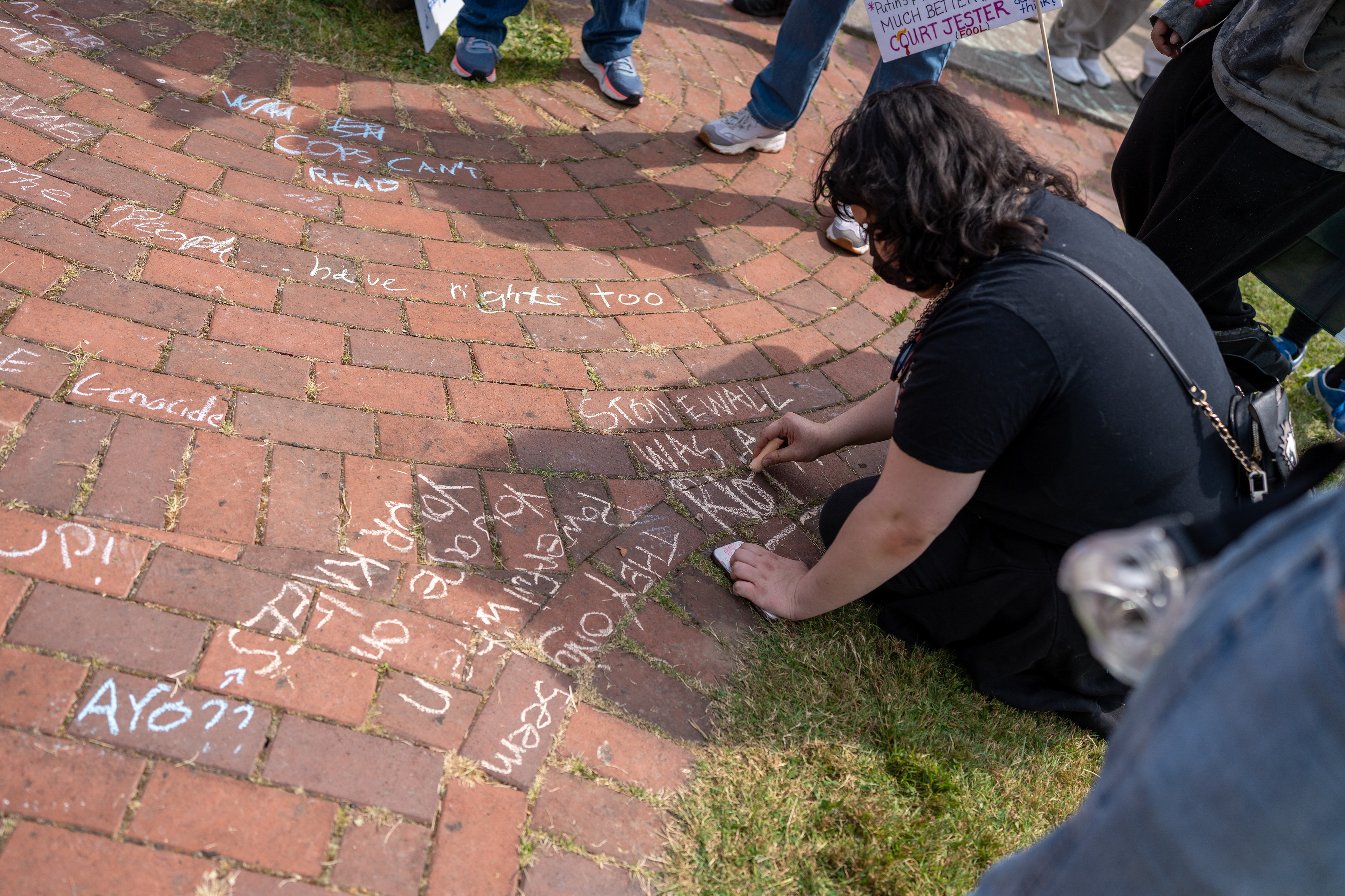 A demonstrator writes “Stonewall was a riot” in chalk on a brick sidewalk at the Twelve Corners intersection during a No Kings protest in Brighton, N.Y., Saturday, June 14, 2025.