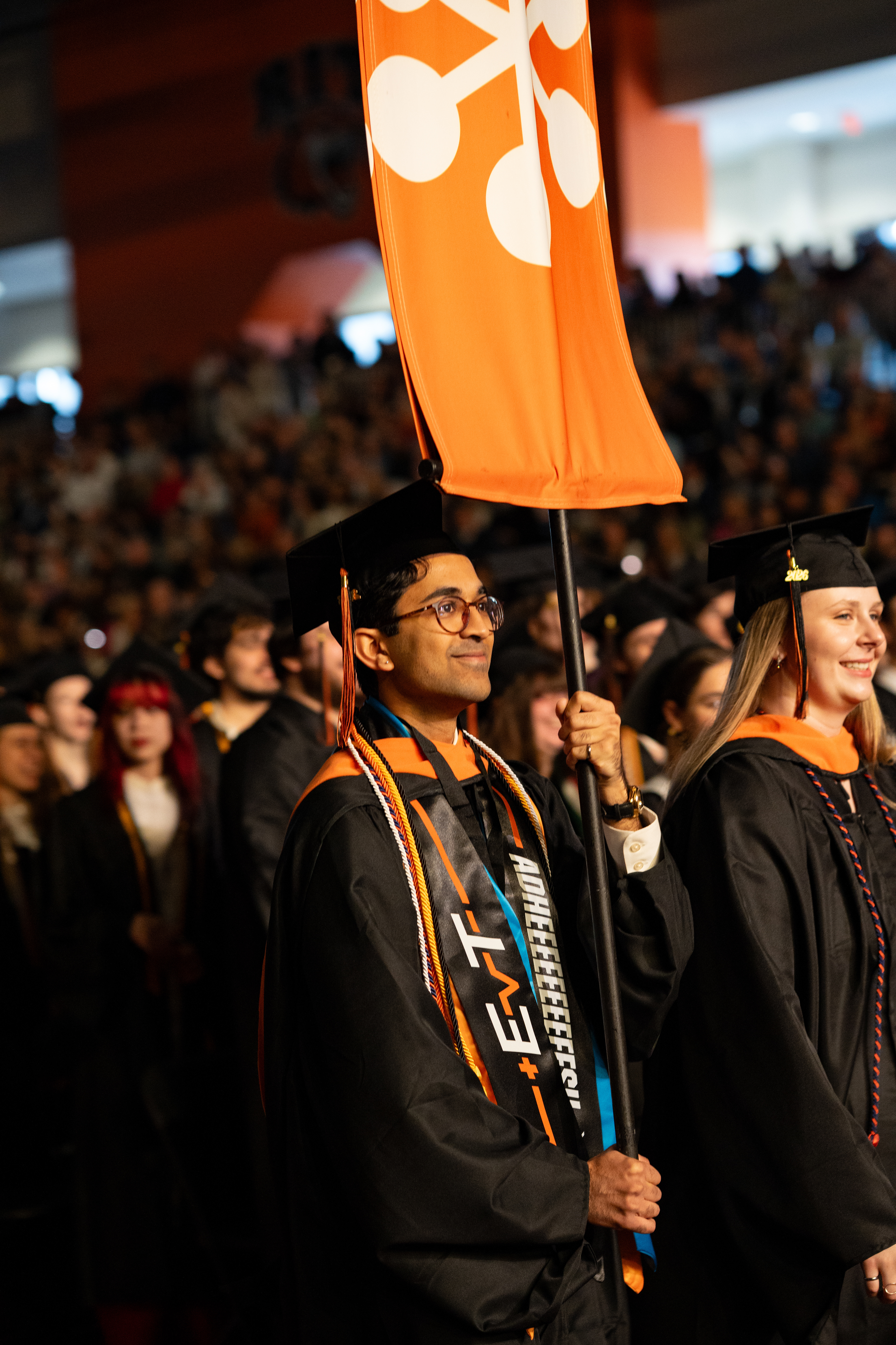 A graduating student carries a college banner during the procession at the 2026 Academic Convocation in the Gordon Field House at the Rochester Institute of Technology in Henrietta, N.Y., Friday, May 8, 2026.