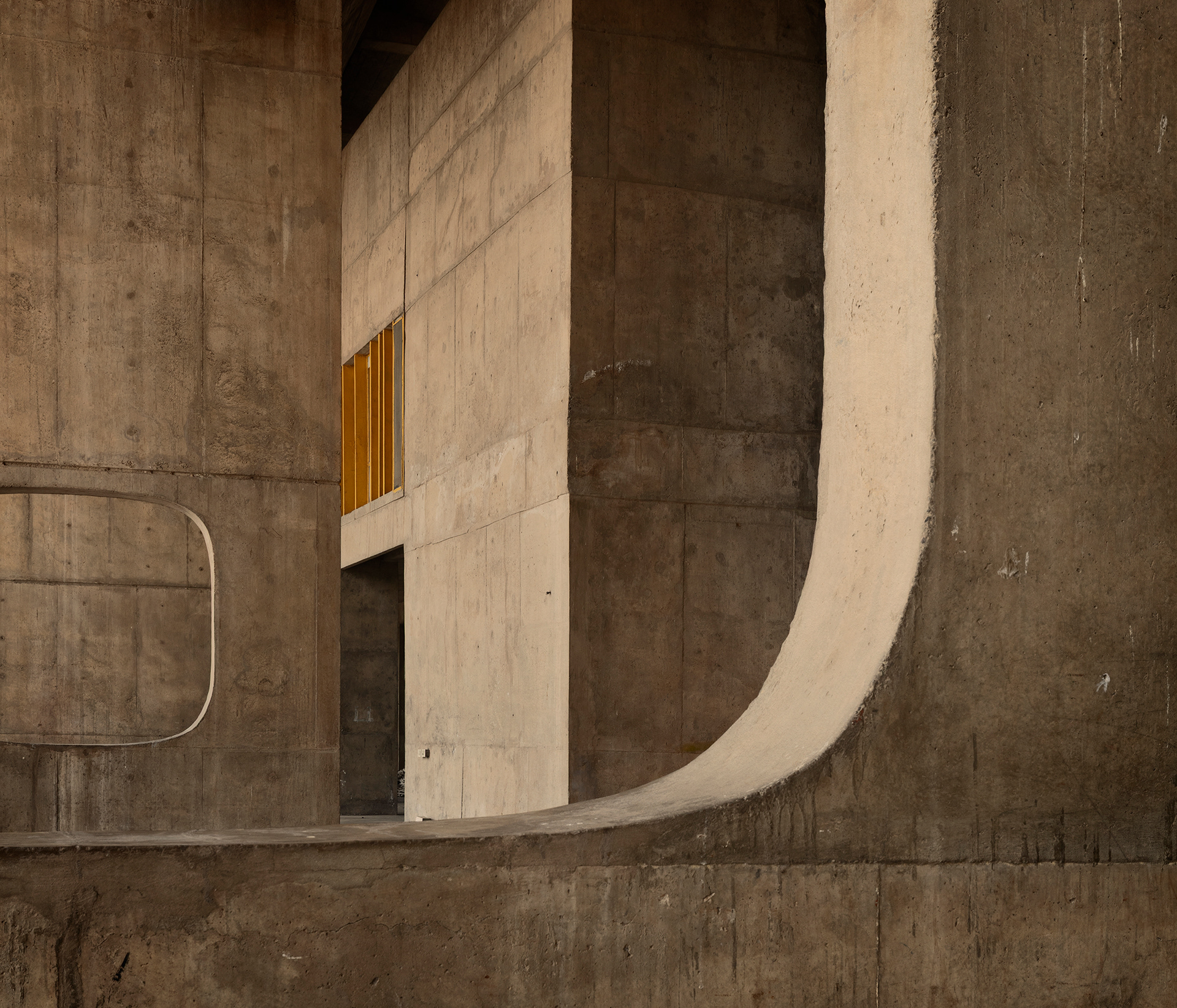 The Palace of Assembly in Chandigarh (1965), designed by Le Corbusier and Pierre Jeanneret, occupies the symbolic centre of the Capitol Complex. Conceived to house the legislative assemblies, the building is organised around two chambers that emerge as autonomous volumes within a vast concrete structure. The hyperbolic paraboloid roof of the main chamber and the curved pyramid protecting the second chamber give the complex a sculptural and almost monumental presence. Between tall columns and intersecting corridors, the architecture creates a sequence of spaces in which power, geometry, and light come together in a profoundly modern language.