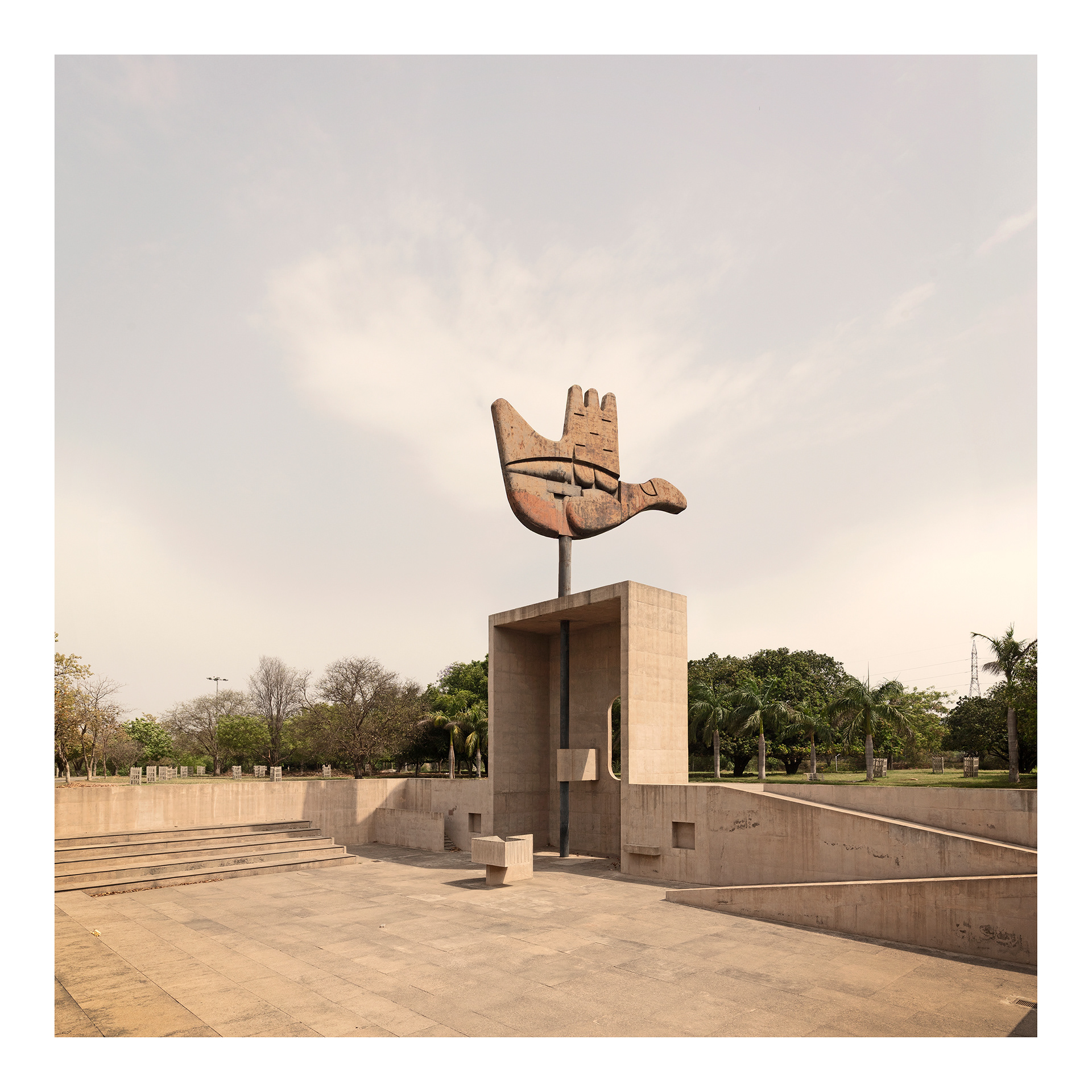 Capitol Complex #1. Fine Art Photographic Inkjet Print 50 x 50 cm. Edition of 3. The Open Hand, conceived by Le Corbusier as a symbol of Chandigarh, is a 14-metre-high bronze sculpture completed in 1985 in the Capitol Complex. Mounted on bearings, the hand turns with the wind, naturally orienting itself towards the square. For Le Corbusier, this open gesture symbolised a fundamental idea: “open to receive, open to give” — a metaphor for sharing, dialogue, and the circulation of people and cultures. Set within a “trench of reflection”, conceived as a space for assembly and public discourse, the sculpture stands as both a political and poetic emblem of the modern city envisioned for independent India.