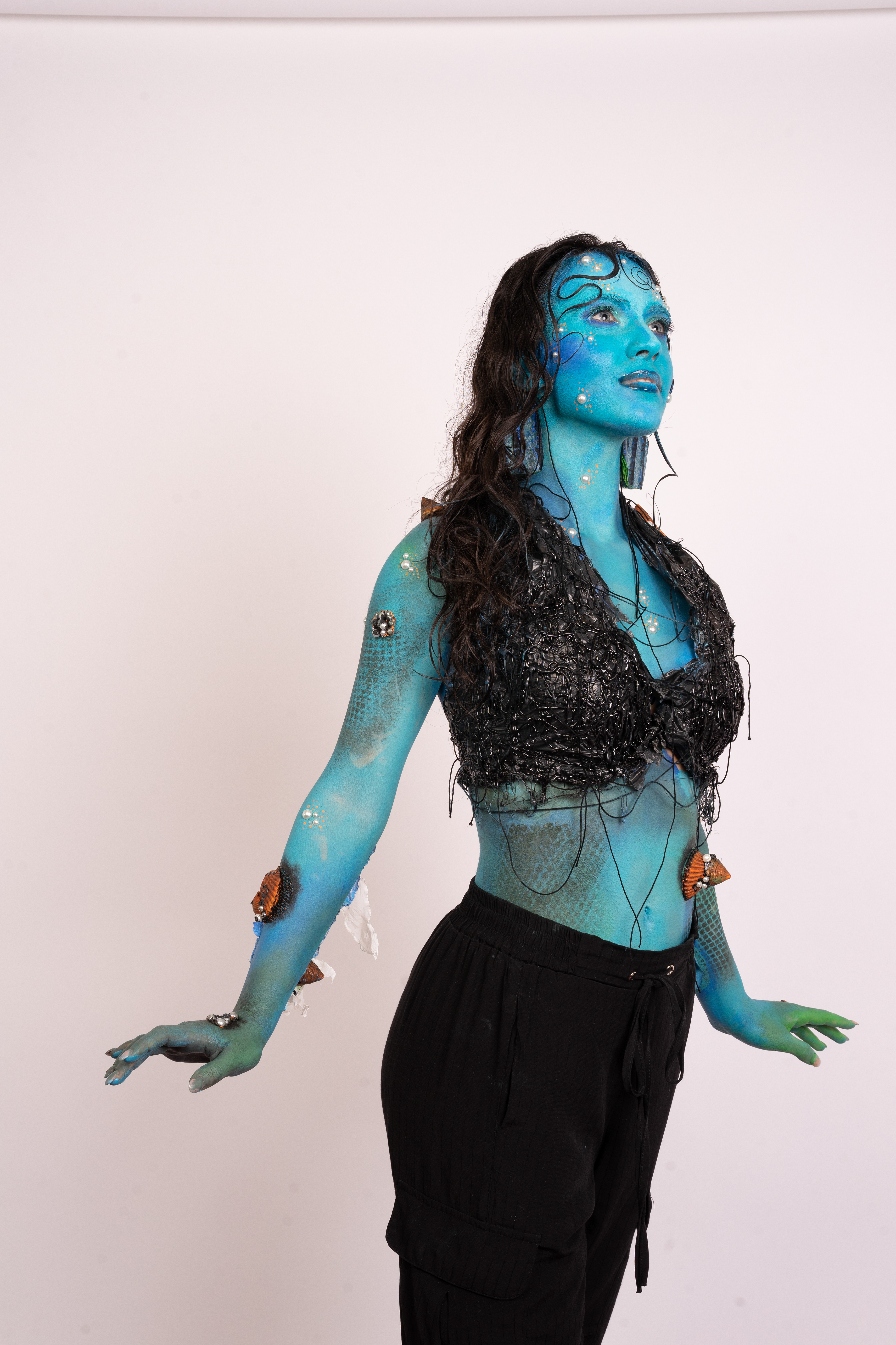 SURVIVED MERMAID Tipologia: Makeup artistico, body painting; Caratteristiche: Il tema di questo progetto è il riciclo. Abbiamo creato una sirena che, per sopravvivere in un mare inquinato, si è fusa con i materiali circostanti, come la plastica. Sono state utilizzate diverse tecniche di bodypainting e makeup artistico. Tutti gli elementi accessori, come pinne, branchie e top, sono stati realizzati utilizzando materiali di scarto; Type: Artistic makeup, body painting; Features: The theme of this project is recycling. We designed a mermaid who, to survive in a polluted sea, has merged with the materials around her, such as plastic. Various body painting and artistic makeup techniques were employed. All accessory elements, including fins, gills, and the top, were made using recycled materials; Makeup hair accessories: Gino Aurora;