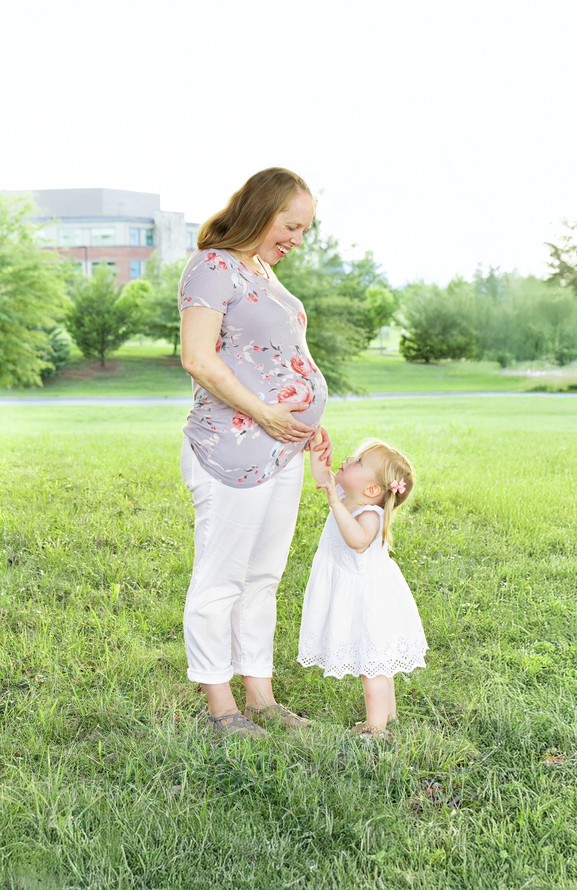 Pastel, light and airy portrait of pregnant mom and daughter in a field next to the hospital
