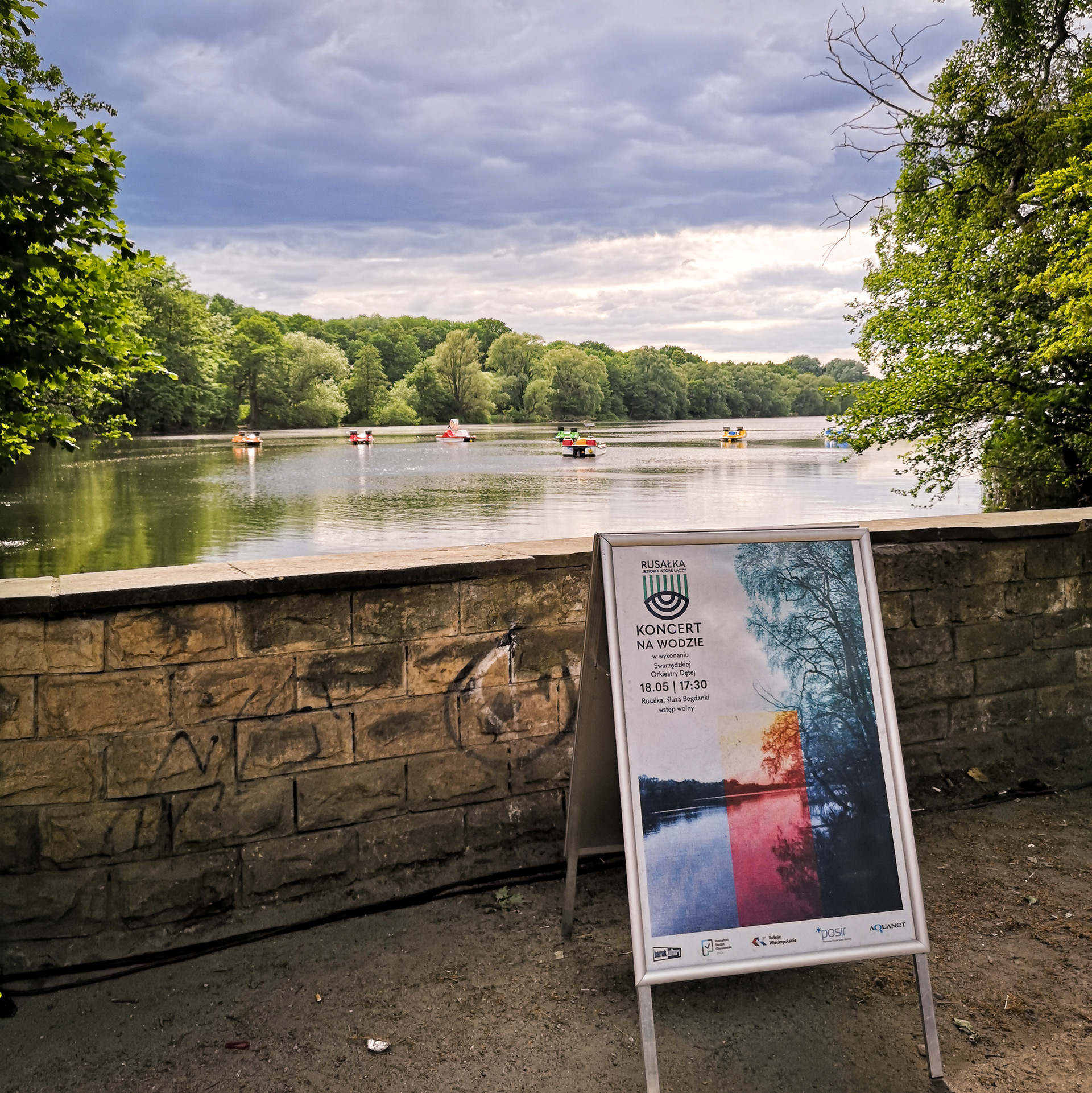 plakat, na jeziorze muzycy w rowerkach wodnych