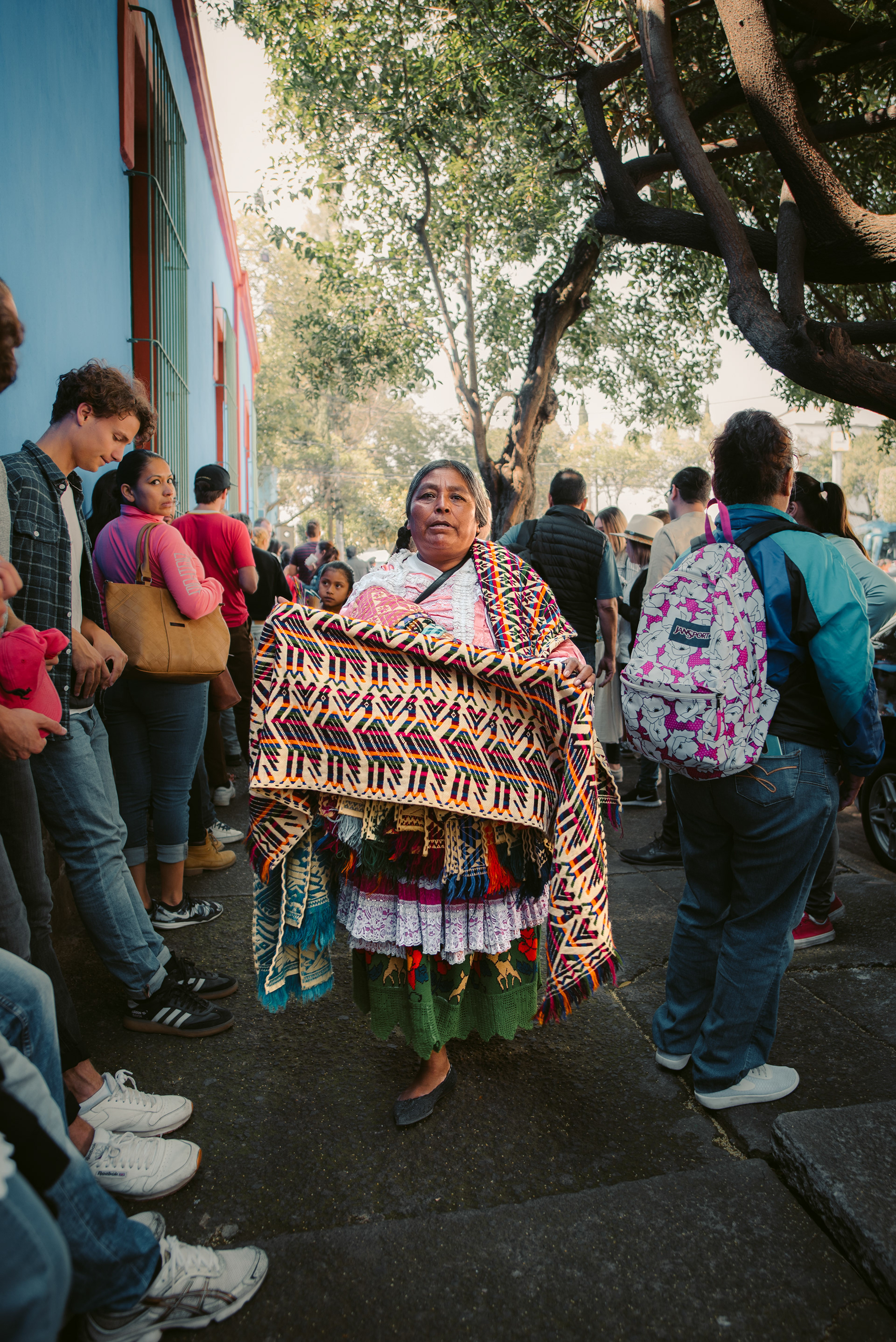 A Mexican woman dressed in traditional attire walked amongst tourists selling Mexican textile