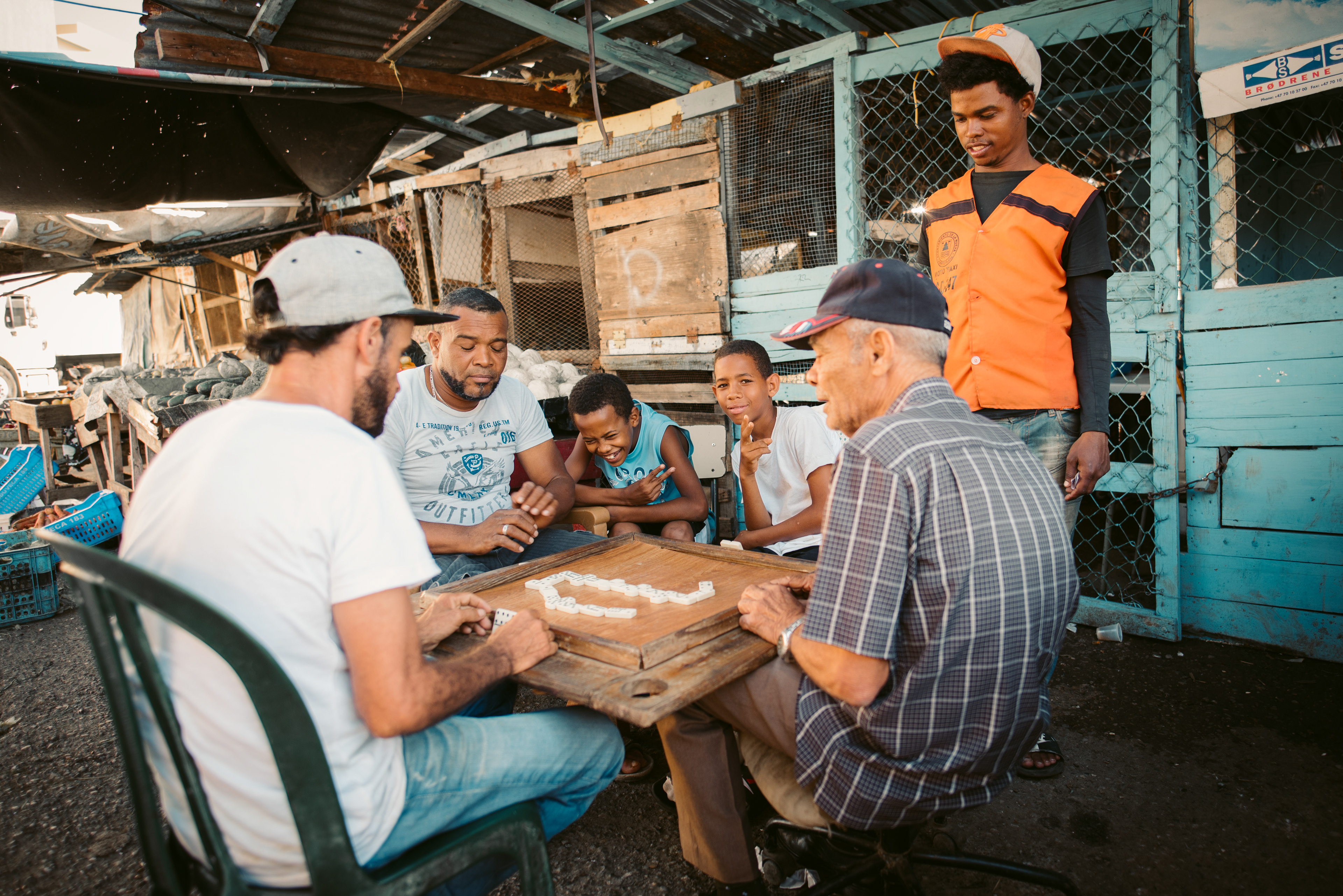 A group of men and children playing Dominoes in the back of an open food market in the Dominican Republic