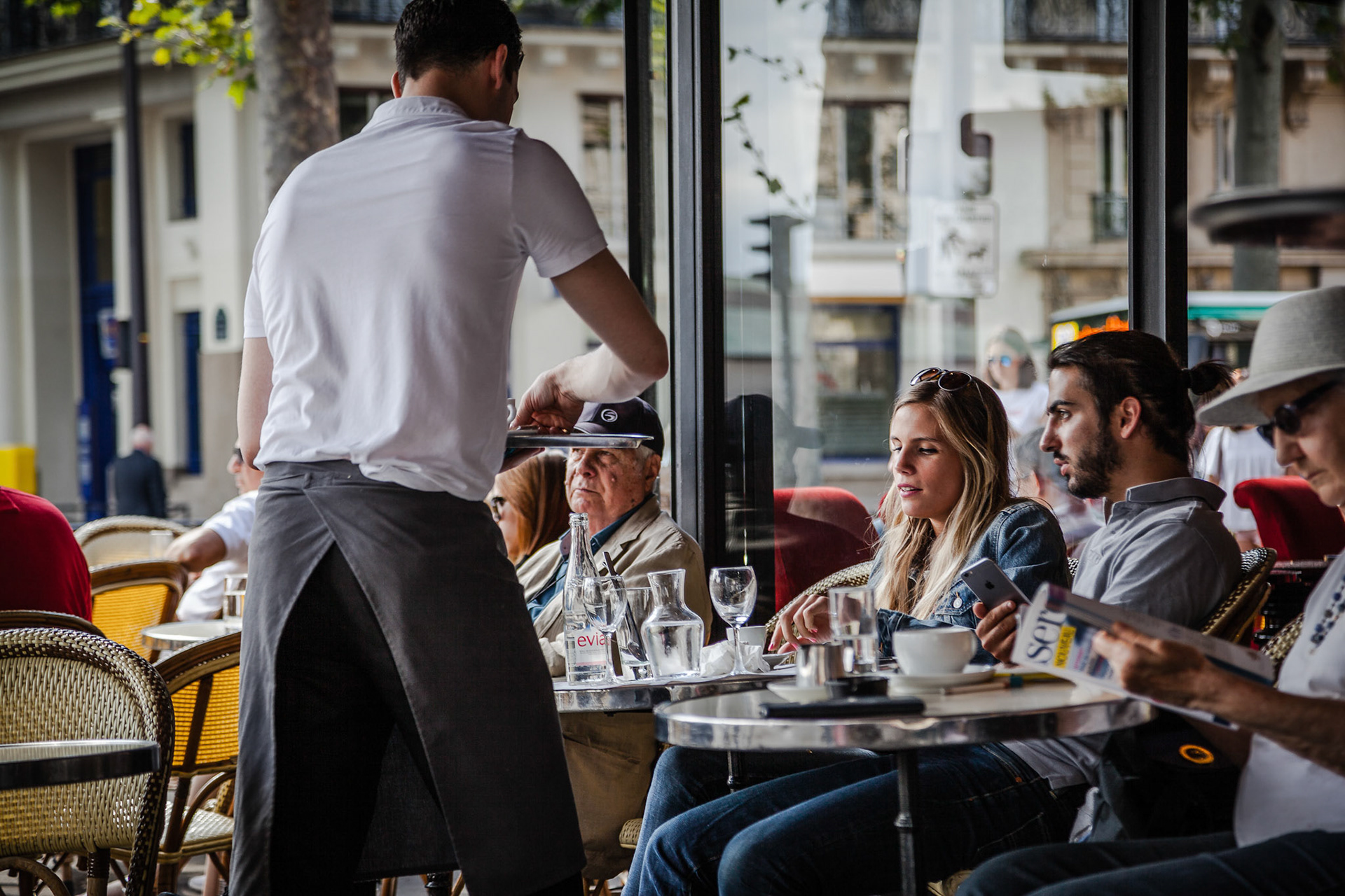 Waiter serving customers at traditional outdoor Parisian cafe in center city.