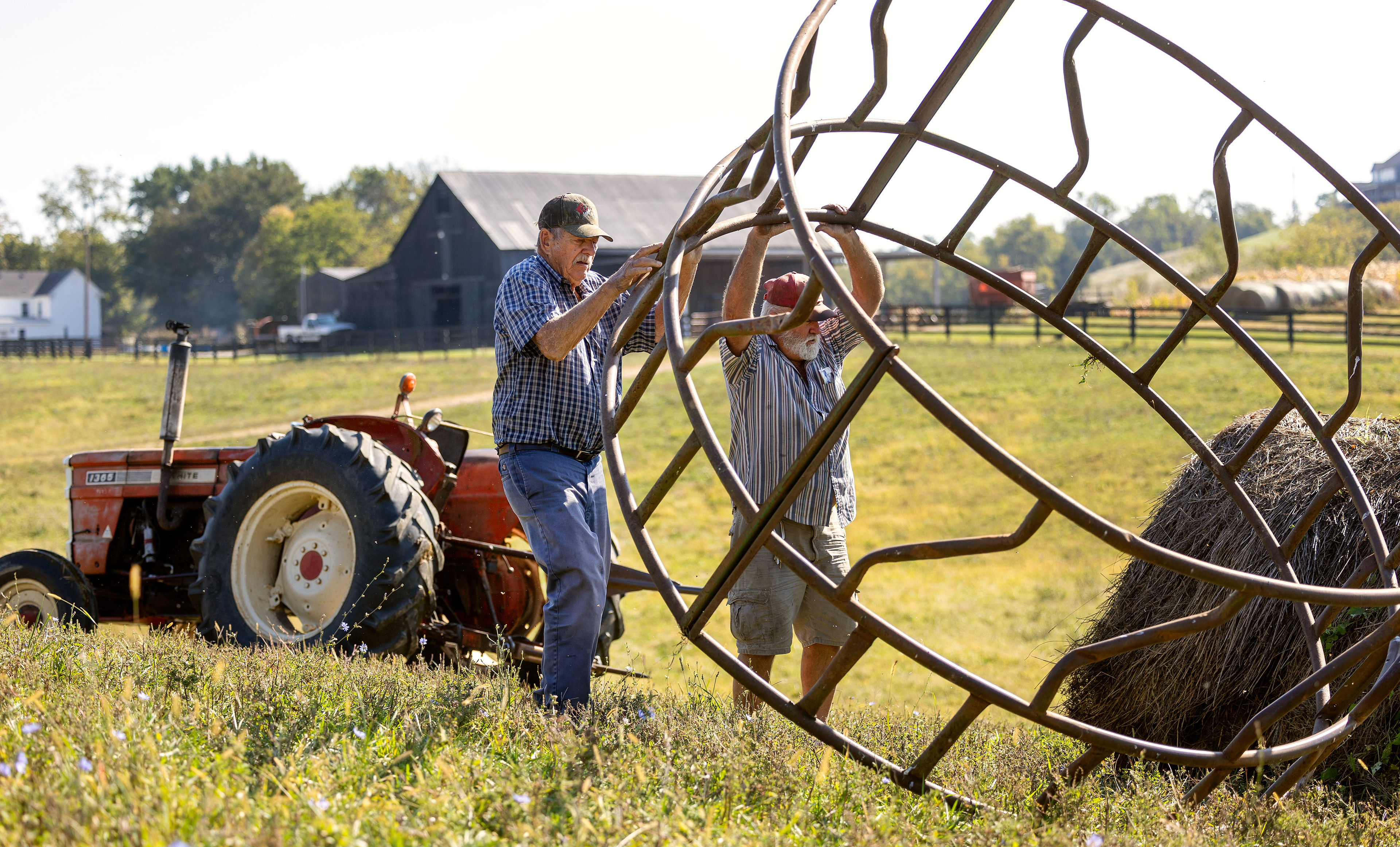 Martin Henson, left, and Don Moore flip a feeder over a hay roll left out in the field for cows to eat from on Thursday Oct. 12, 2023. in Franklin County, Kentucky Photo by Matthew Mueller
