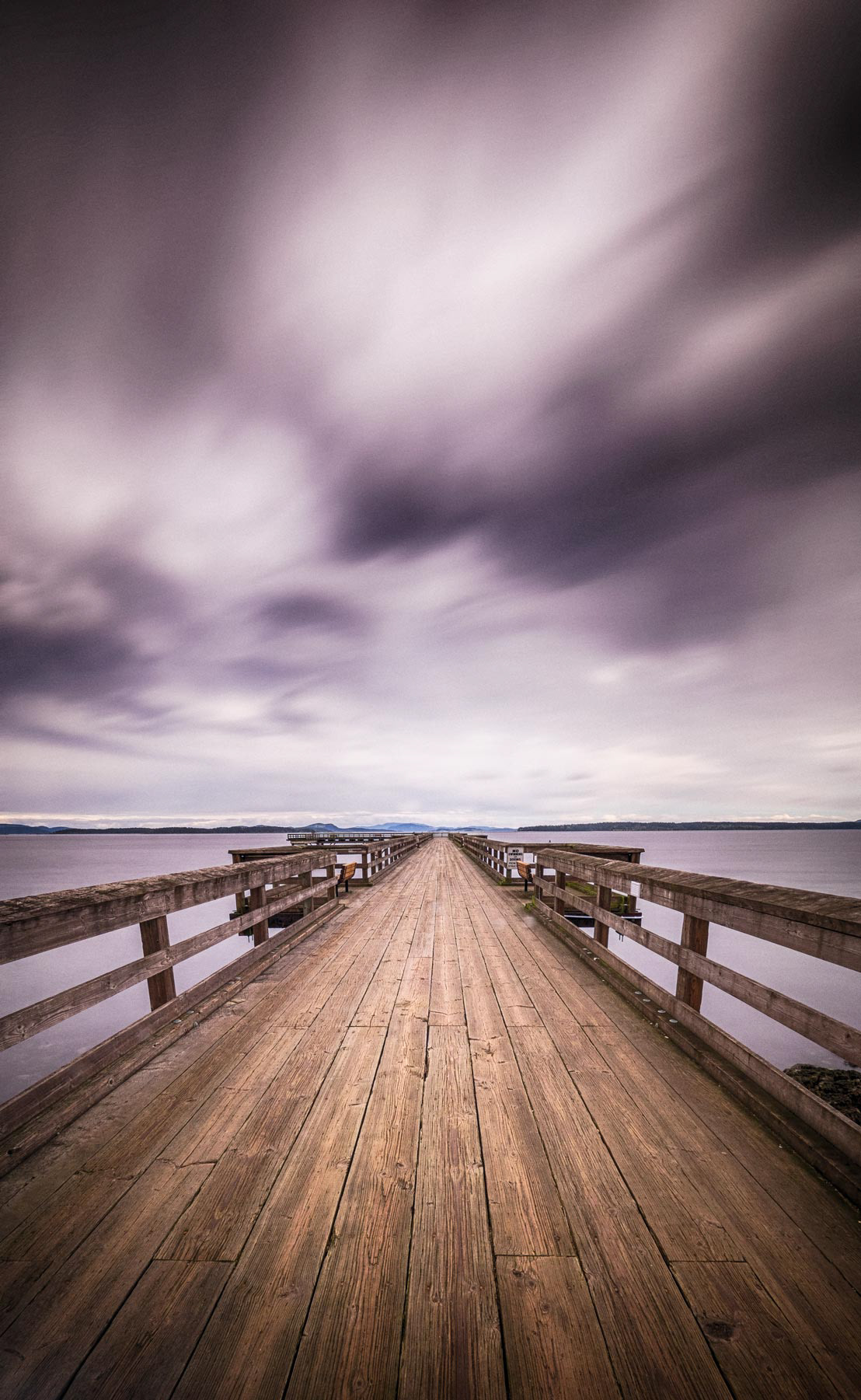 dark clouds, pregnant with rain, shredding across the sky above empty pier stretching out to the horizon.