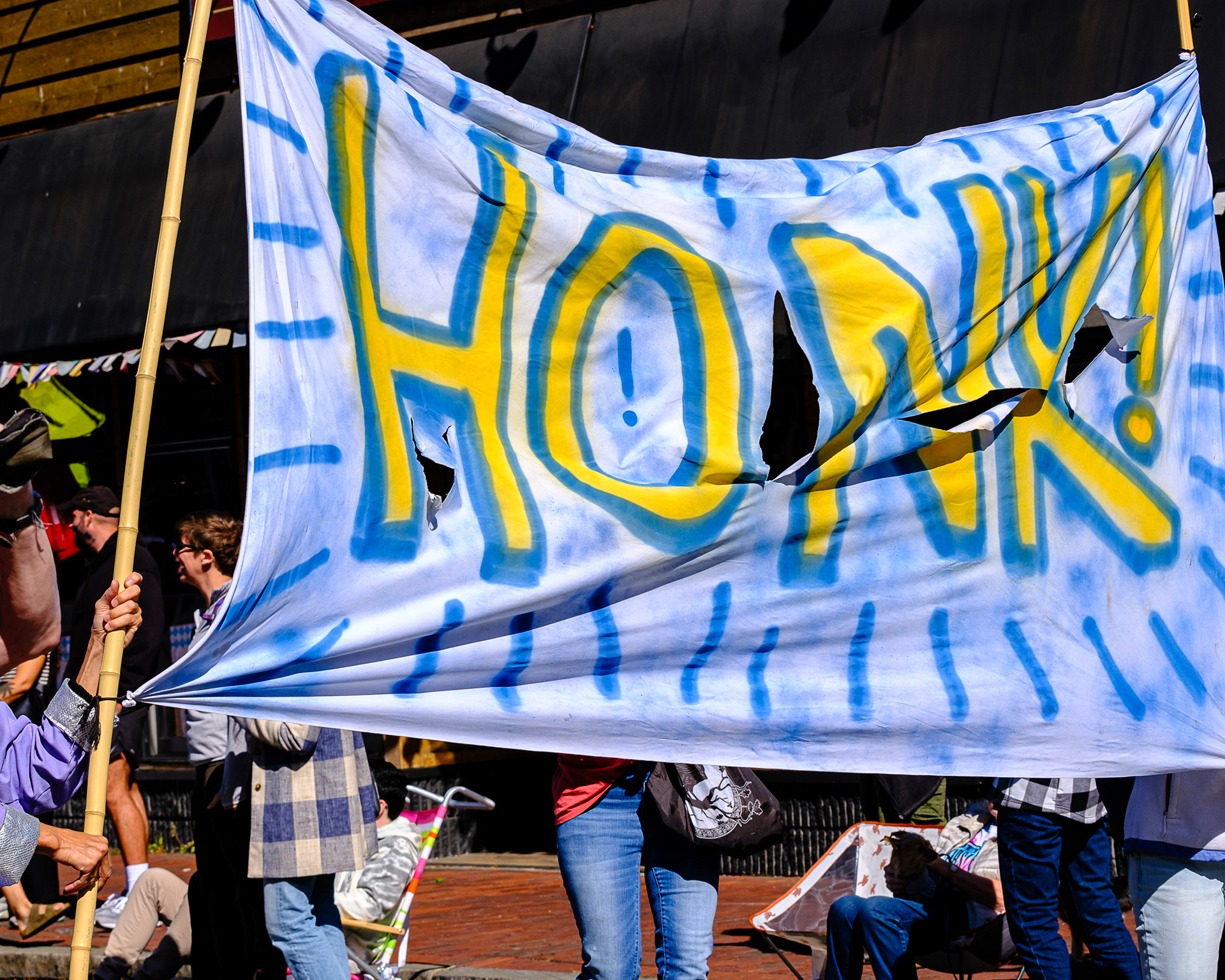 People carrying a homemade banner that reads "HONK!" in spraypaint.