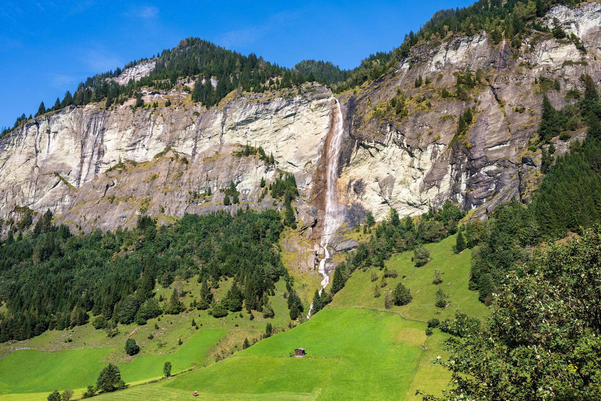 A tall waterfall cascades over a high rocky mountain in the Austrian Alps.