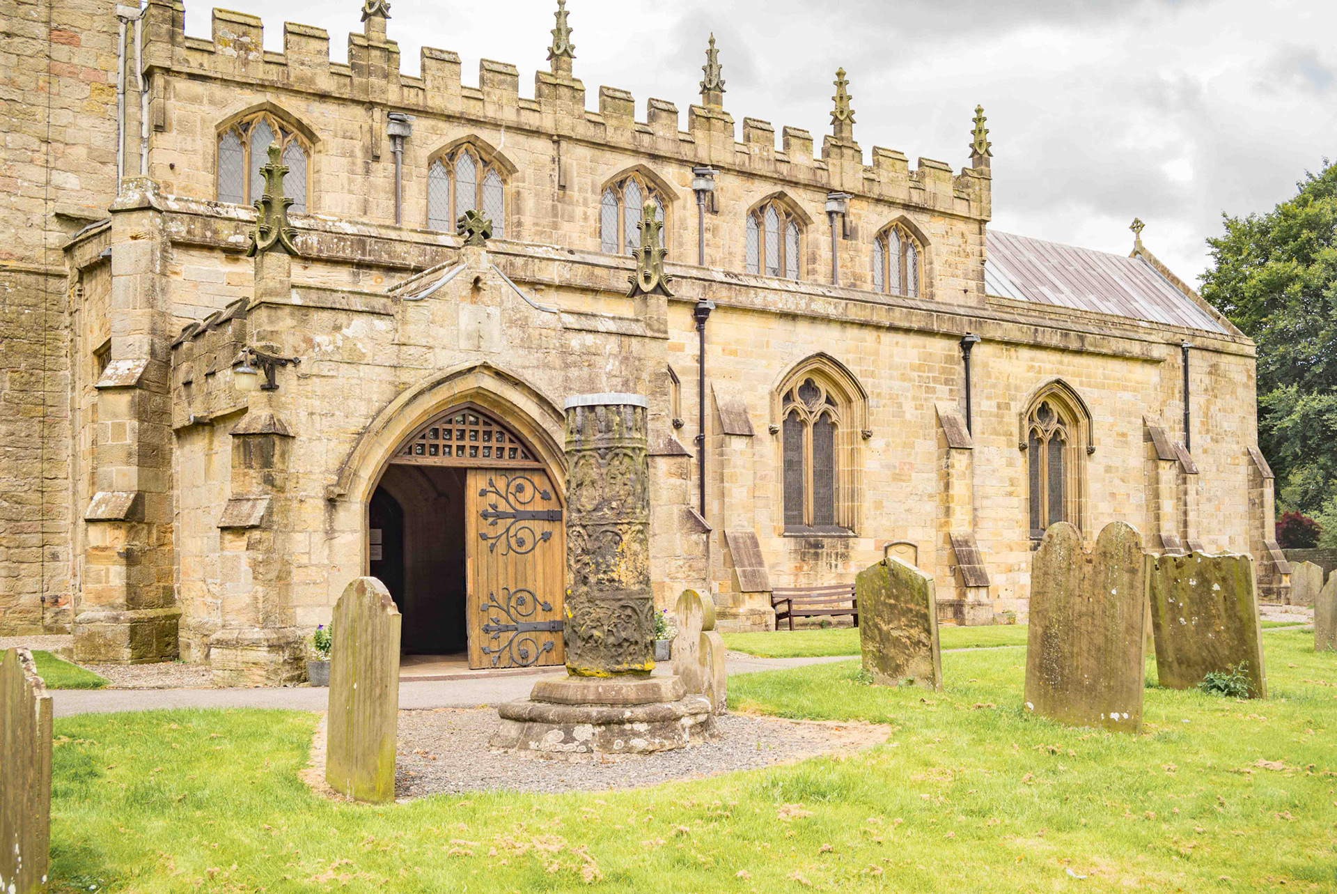 Ancient Cross remains distance view showing the Church - St Mary's Church  Masham North Yorkshire UK 2024