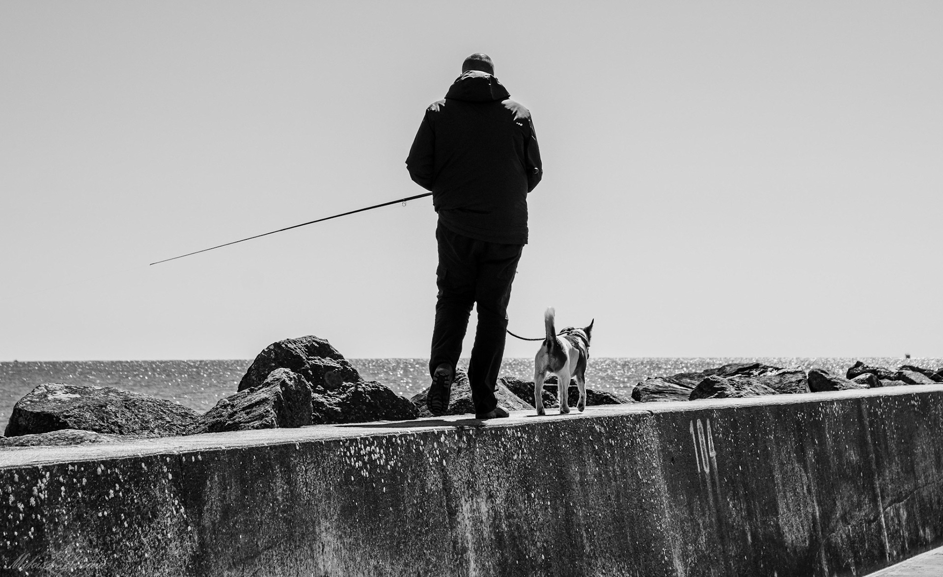 Un pêcheur à la ligne et son petit chien sur la digue du chenal du port de Saint Gilles Croix de Vie, photo noir et blanc 12
