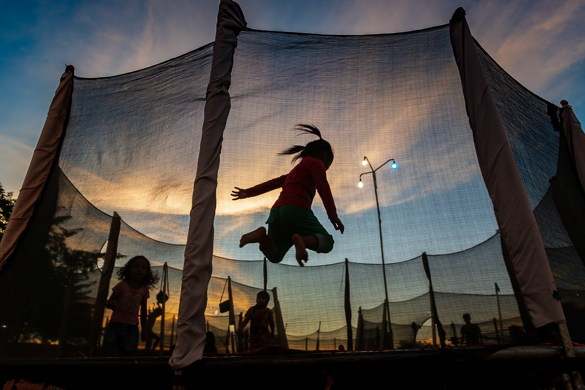 In the night market on the edge of Siem Reap, a young girl let's loose, jumping with friends on a trampoline with the exuberance that only children have.